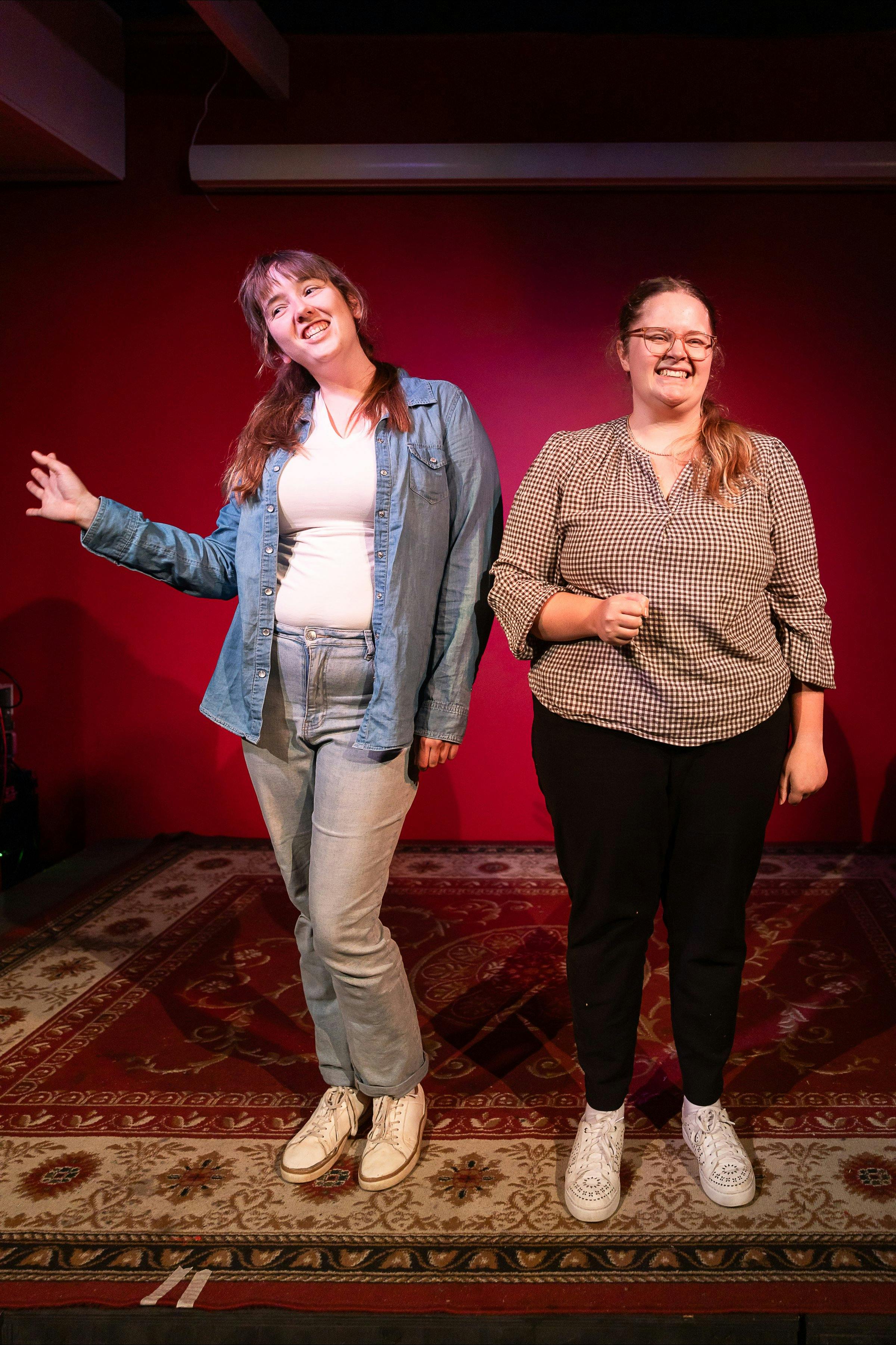 Two young women stand on stage side by side, smiling, as if giving a presentation.