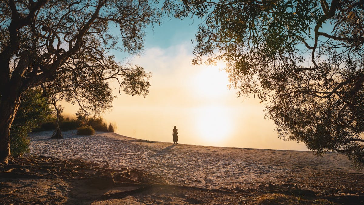 Woman standing by Brown Lake Bummiera at sunset on Minjerribah.