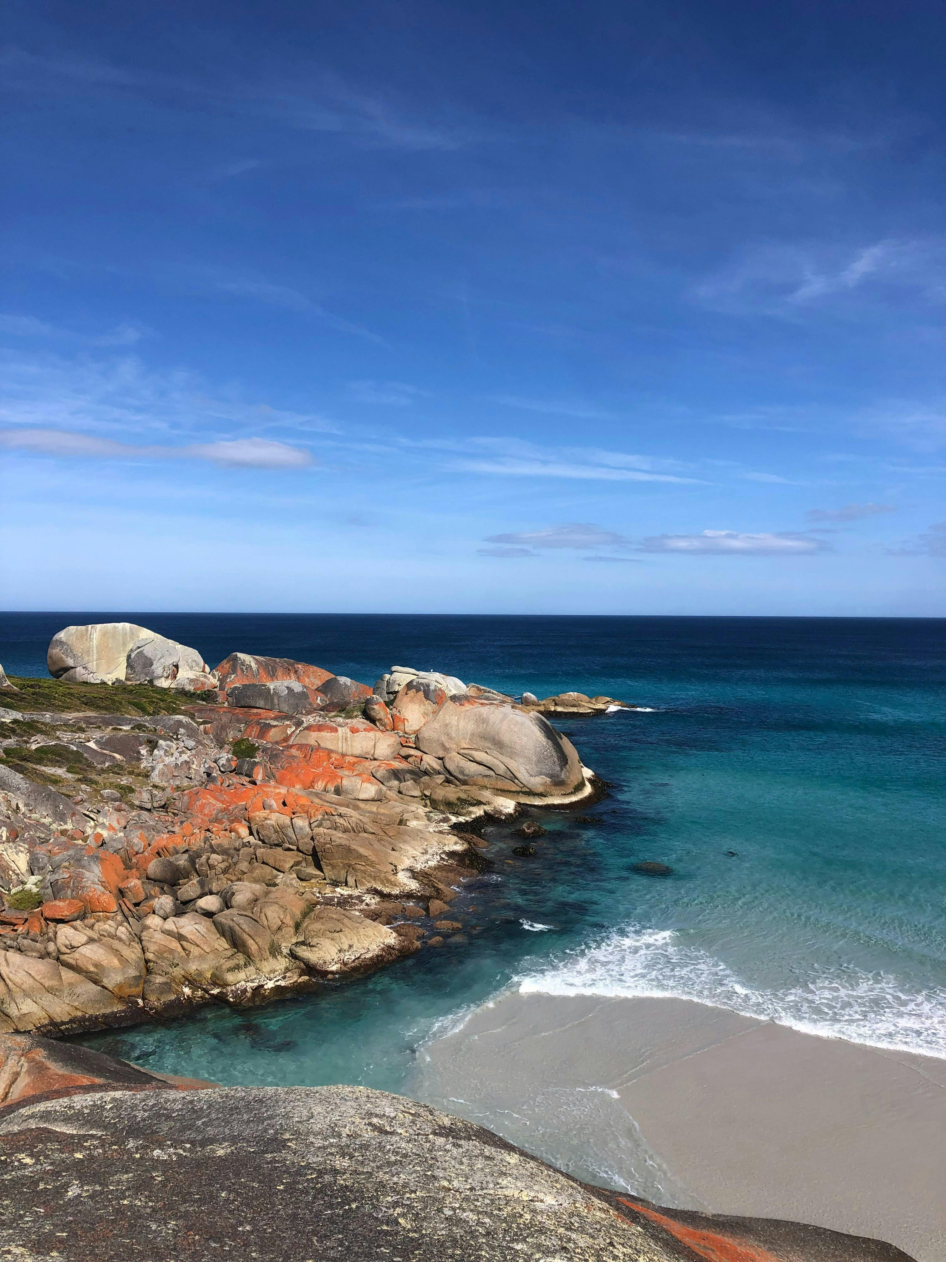 Orange lichen covered rocks and turquoise water at Bay of Fires Tasmania coastal walking trail.