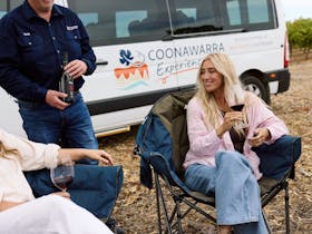 Coonawarra Experiences host pouring wine for guests relaxing by the van in a vineyard setting.