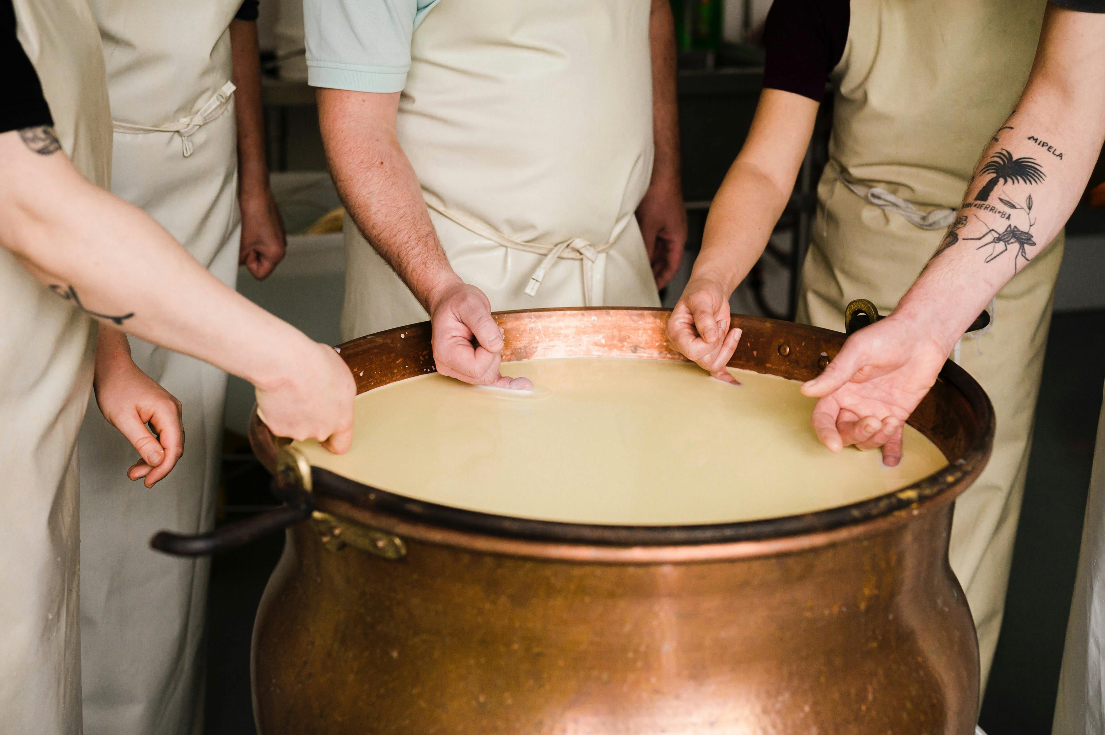 Students arms and fingers shown  testing milk in a copper vat