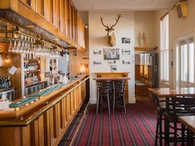 Bar interior with stools, wooden decor, and a tartan-patterned carpet.