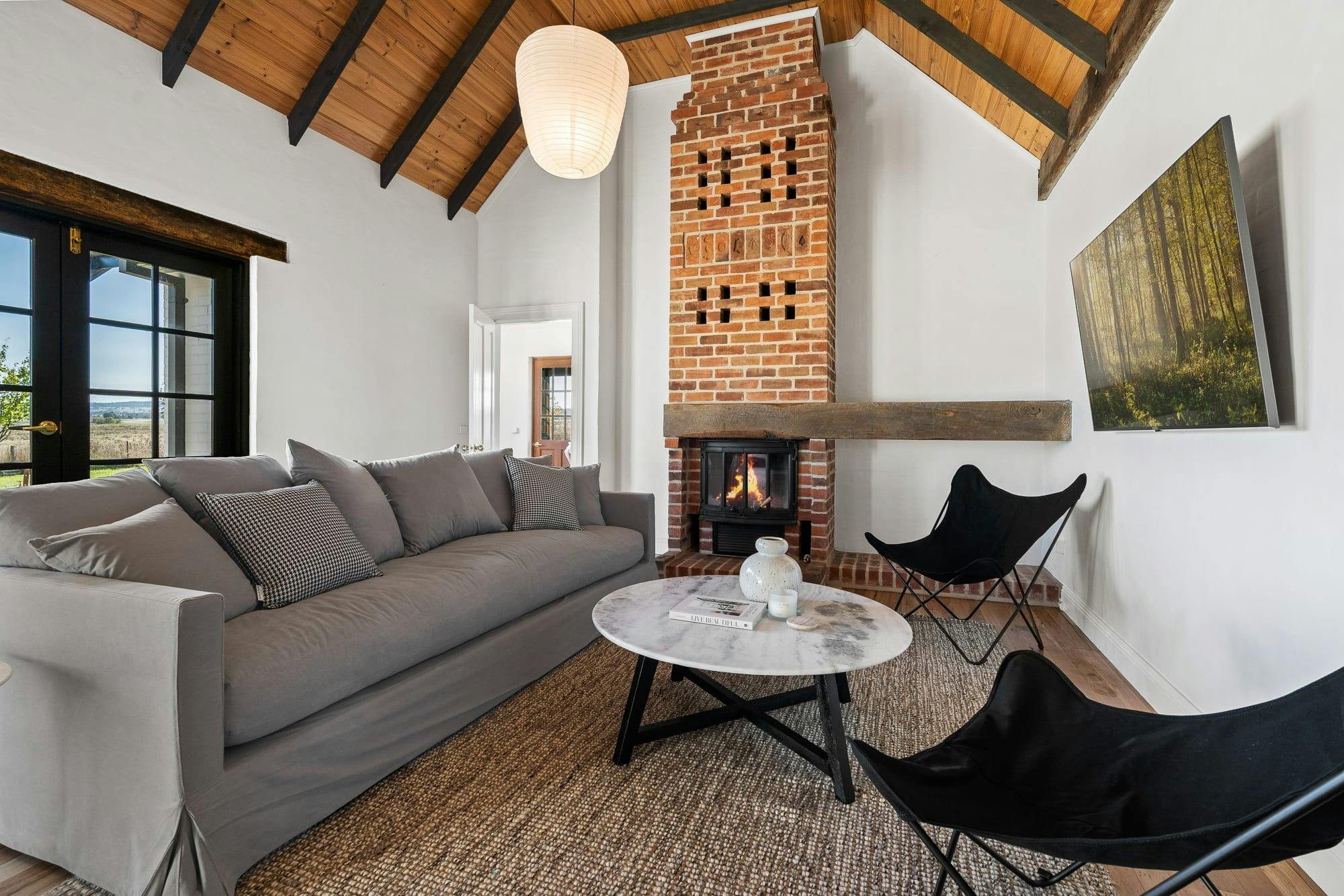 Living room with grey couch, 2 black arm chairs, fire place, tv on the wall