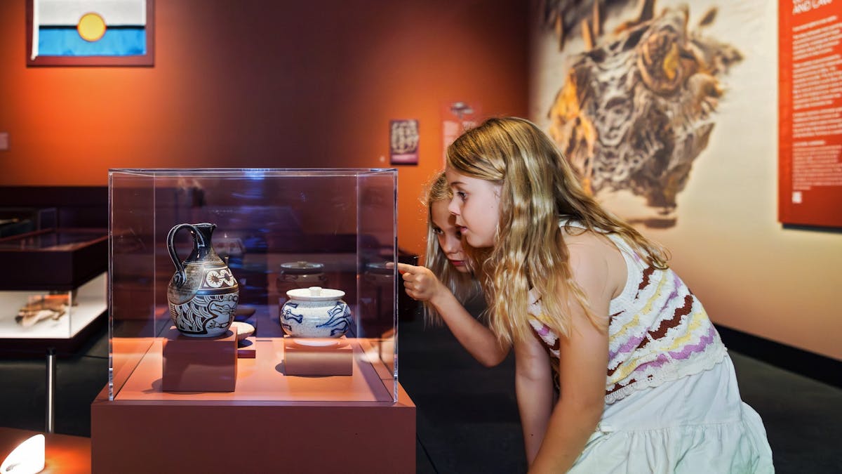 Two children kneel down to point and look at pottery objects decorated with crocodile designs Two children kneel down to point and look at pottery objects decorated with crocodile designs