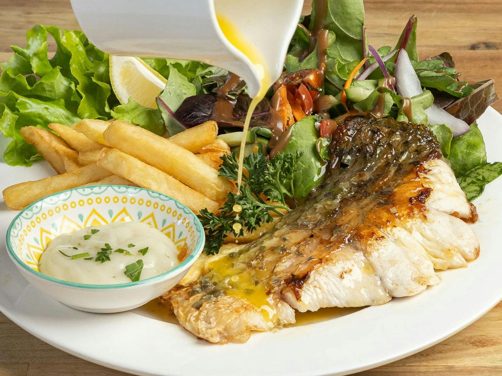 Grilled fish with chips and sauce being poured over