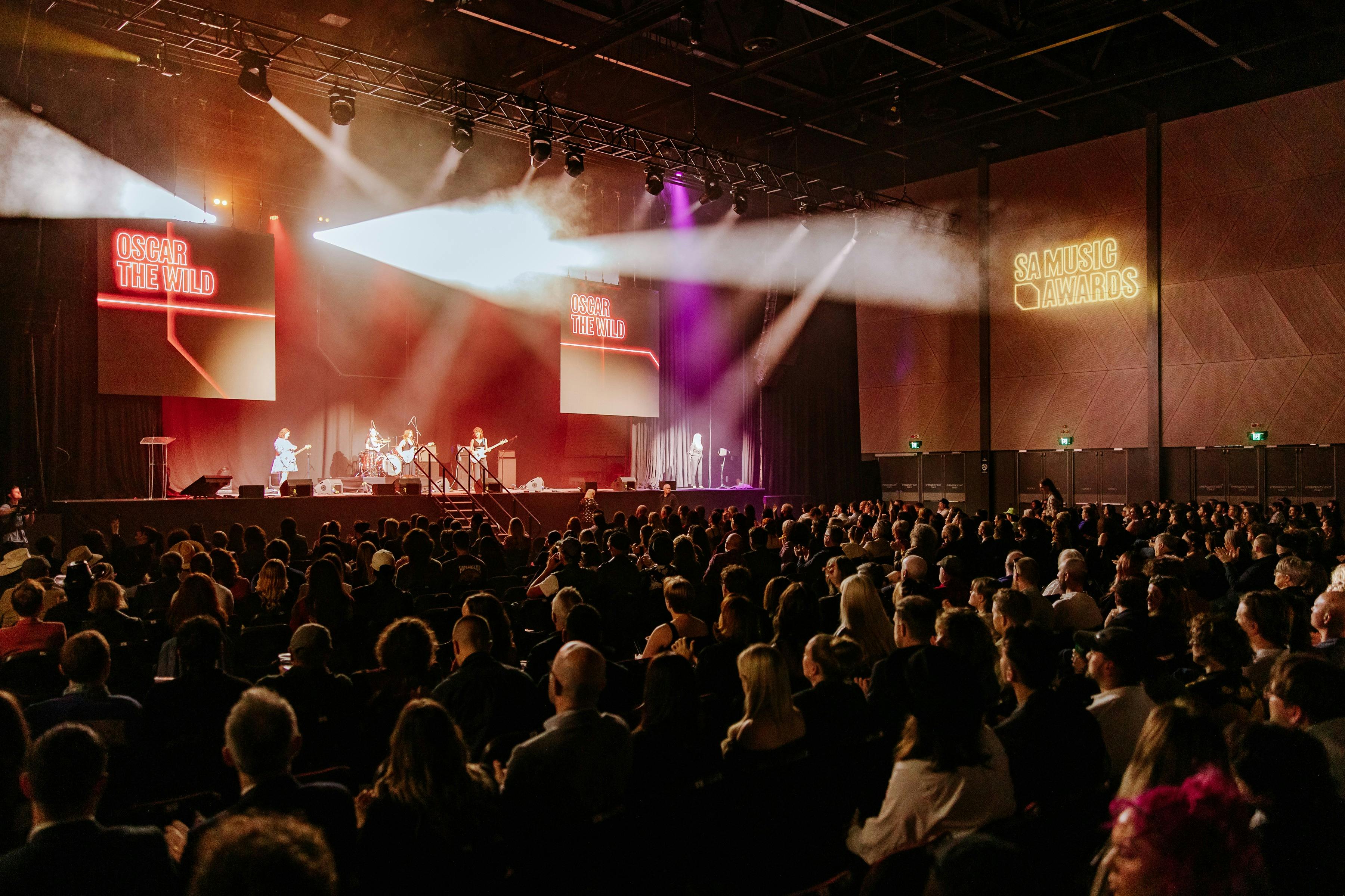 Crowded audience watches a live awards ceremony as musicians perform onstage under spotlights.