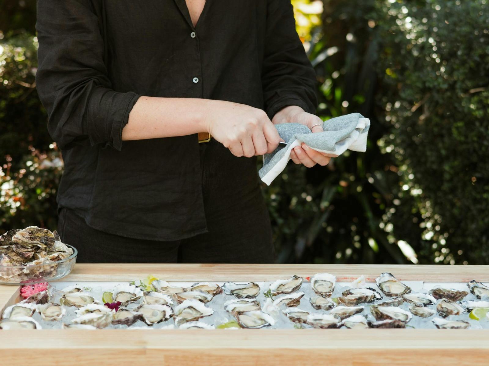 Two hands expertly shuck an oyster at an outdoor chilled oyster bar