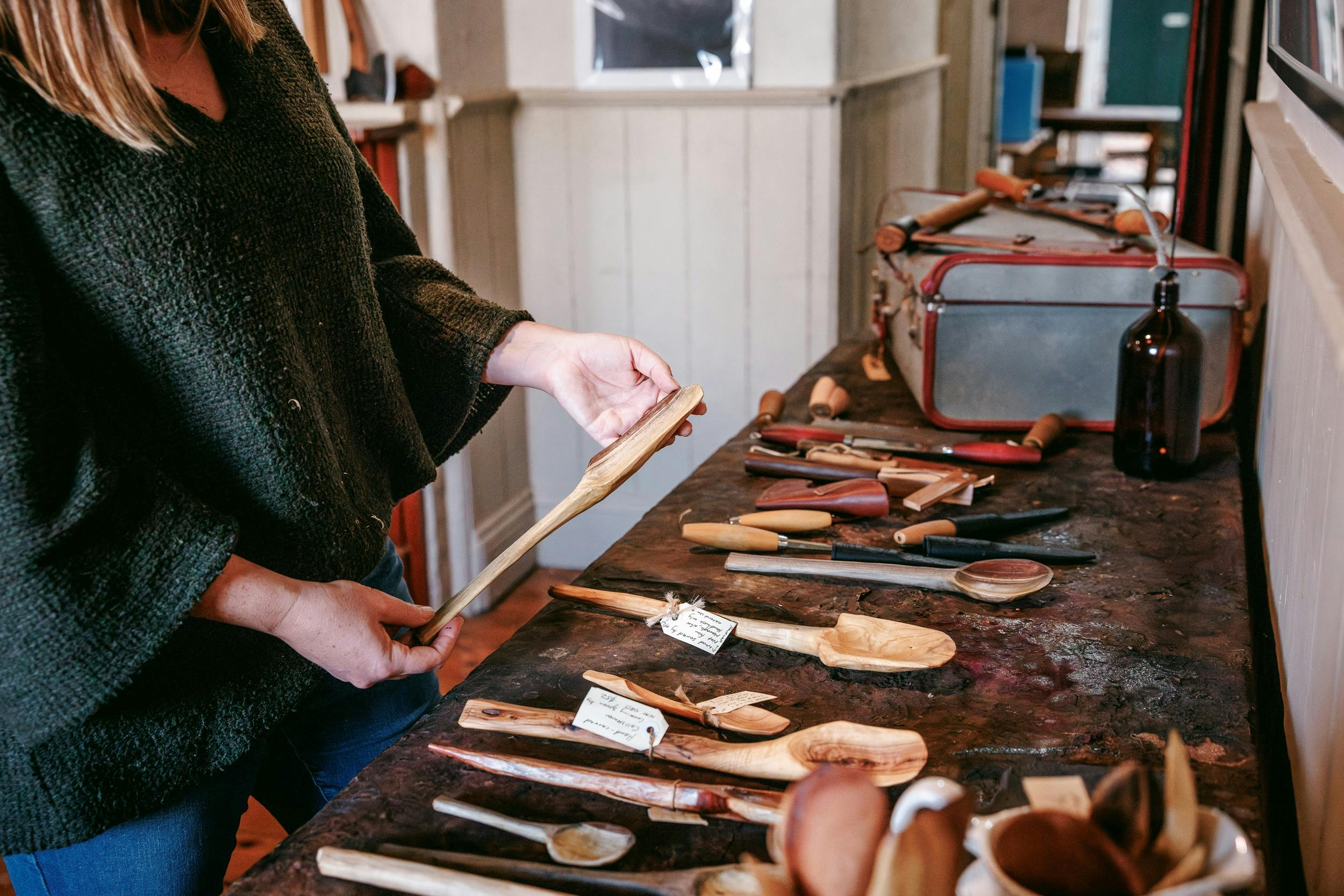 a woman picking up a finished wooden spoon