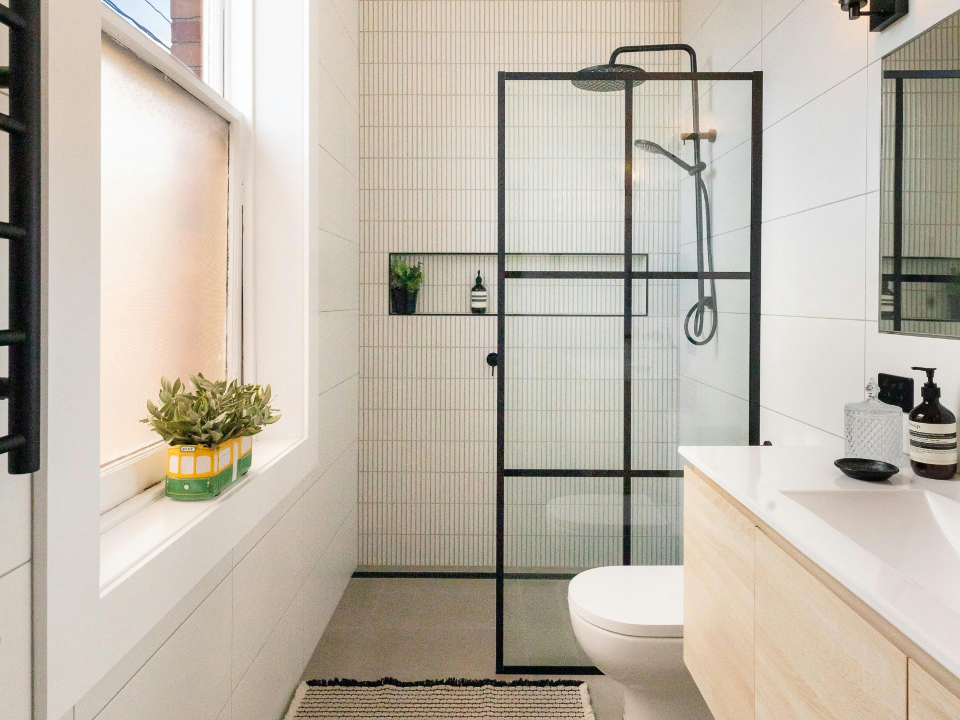 Stylish bathroom, white tiles, glass shower screen with black dividers, rain shower head