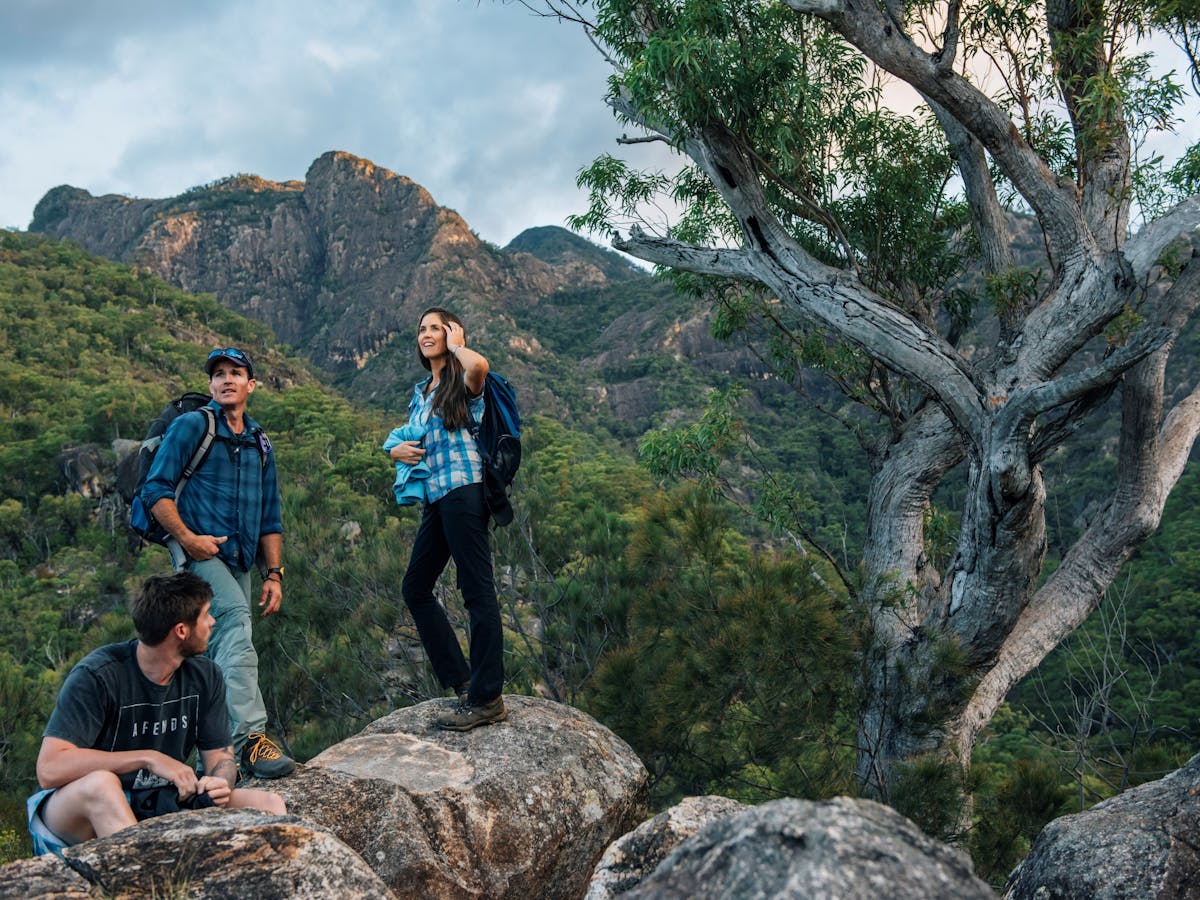 Three hikers stand on large boulders with a mountain range behind them Three hikers stand on large boulders with a mountain range behind them