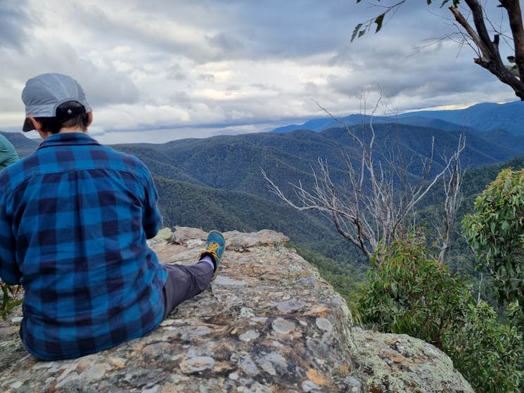 woman sits at lookout overlooking wilderness ridges and gullies