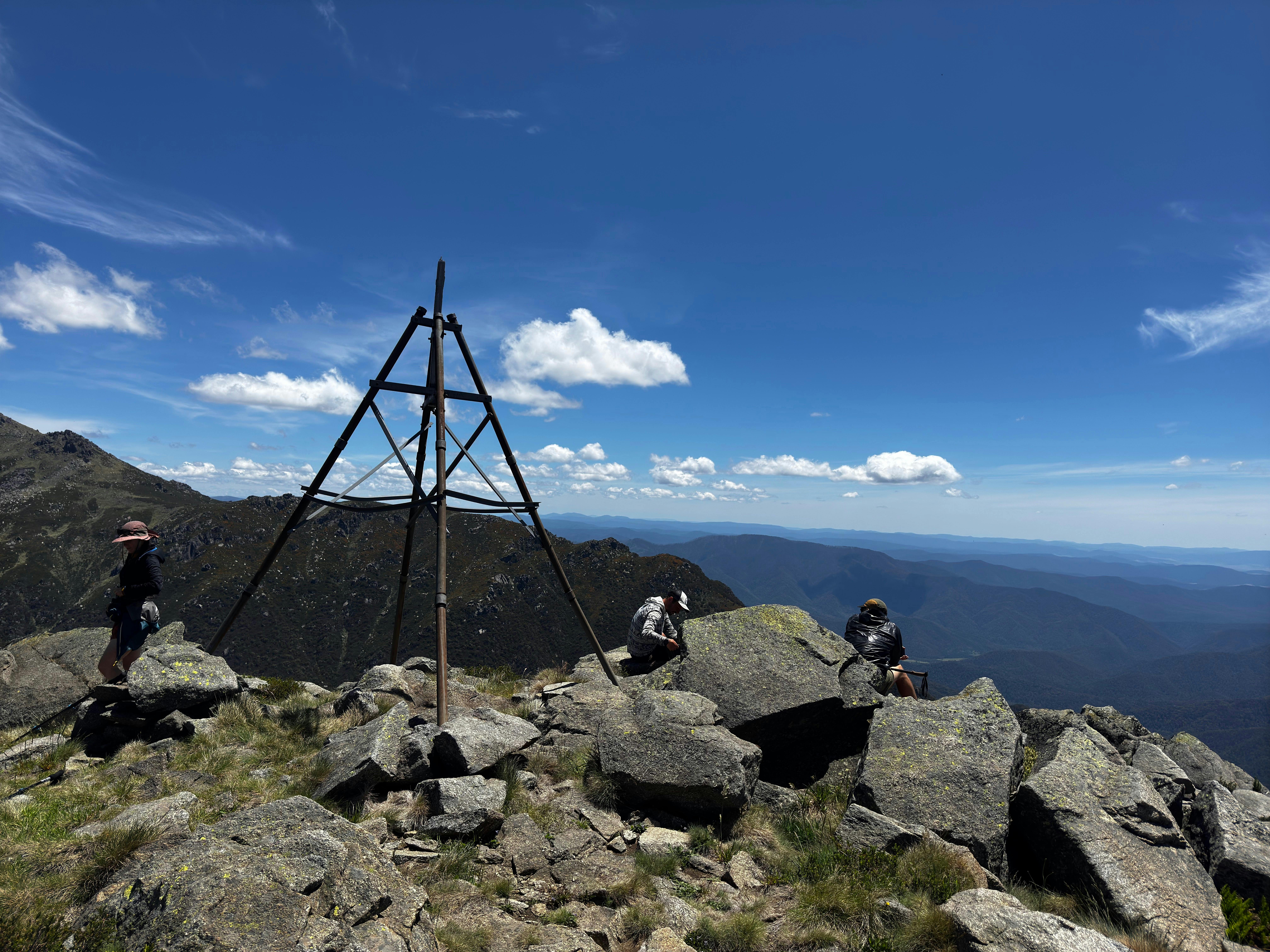 Three hikers at the top of a mountain looking at the view.