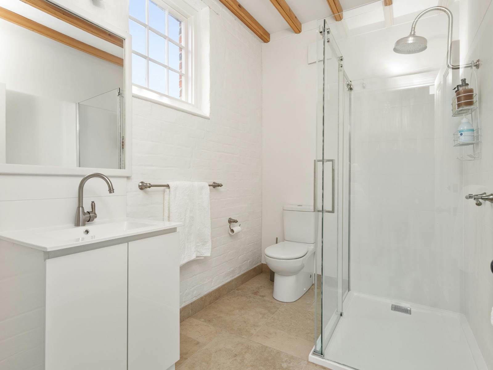 White bathrrom with stone floor tiles, white sink, toilet and shower