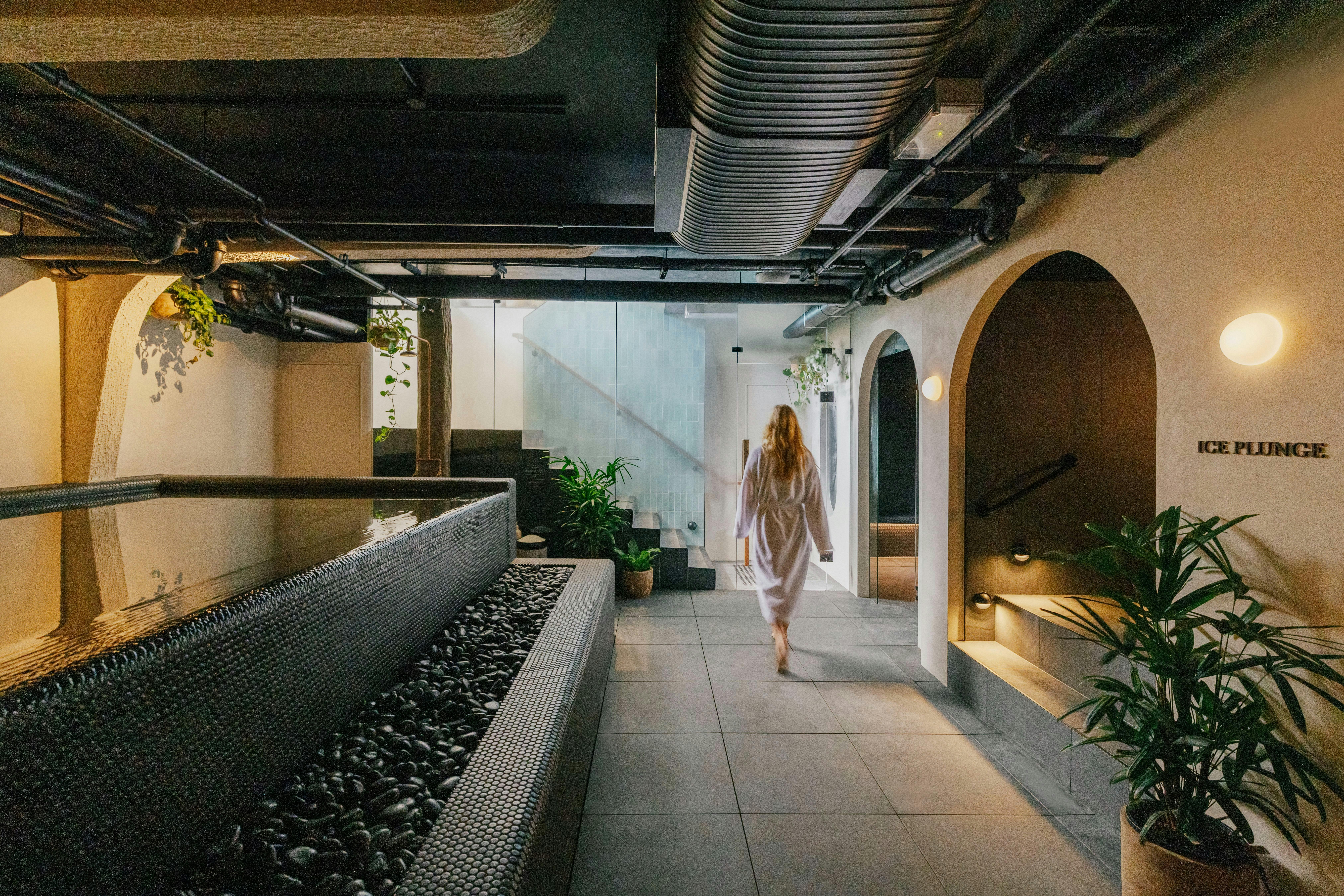 A robed woman walking past the mineral hot pool and arched walls of the bathhouse.