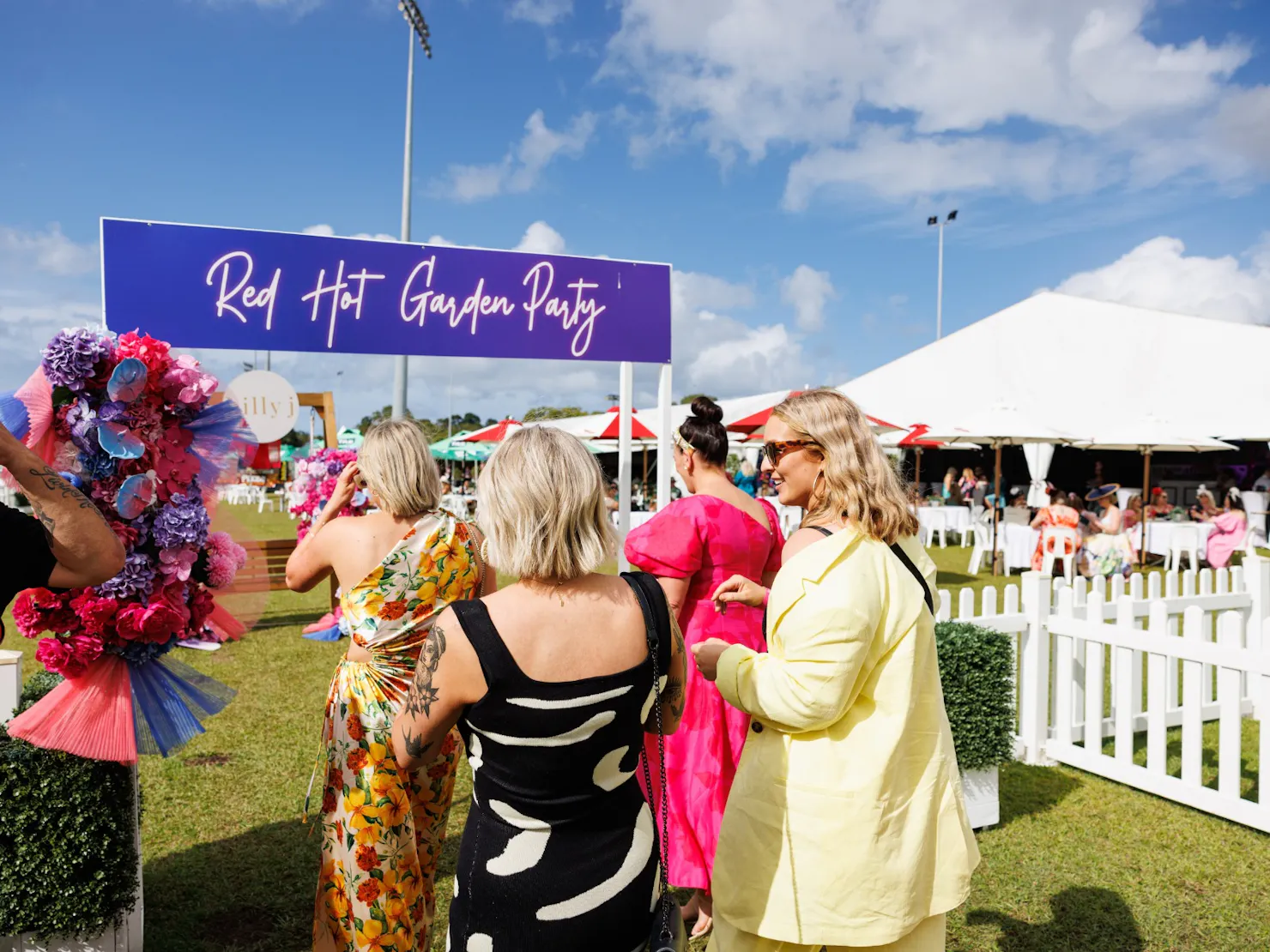 Group of ladies waking into a fenced off marquee area under an arbour sign - Red Hot Garden Party