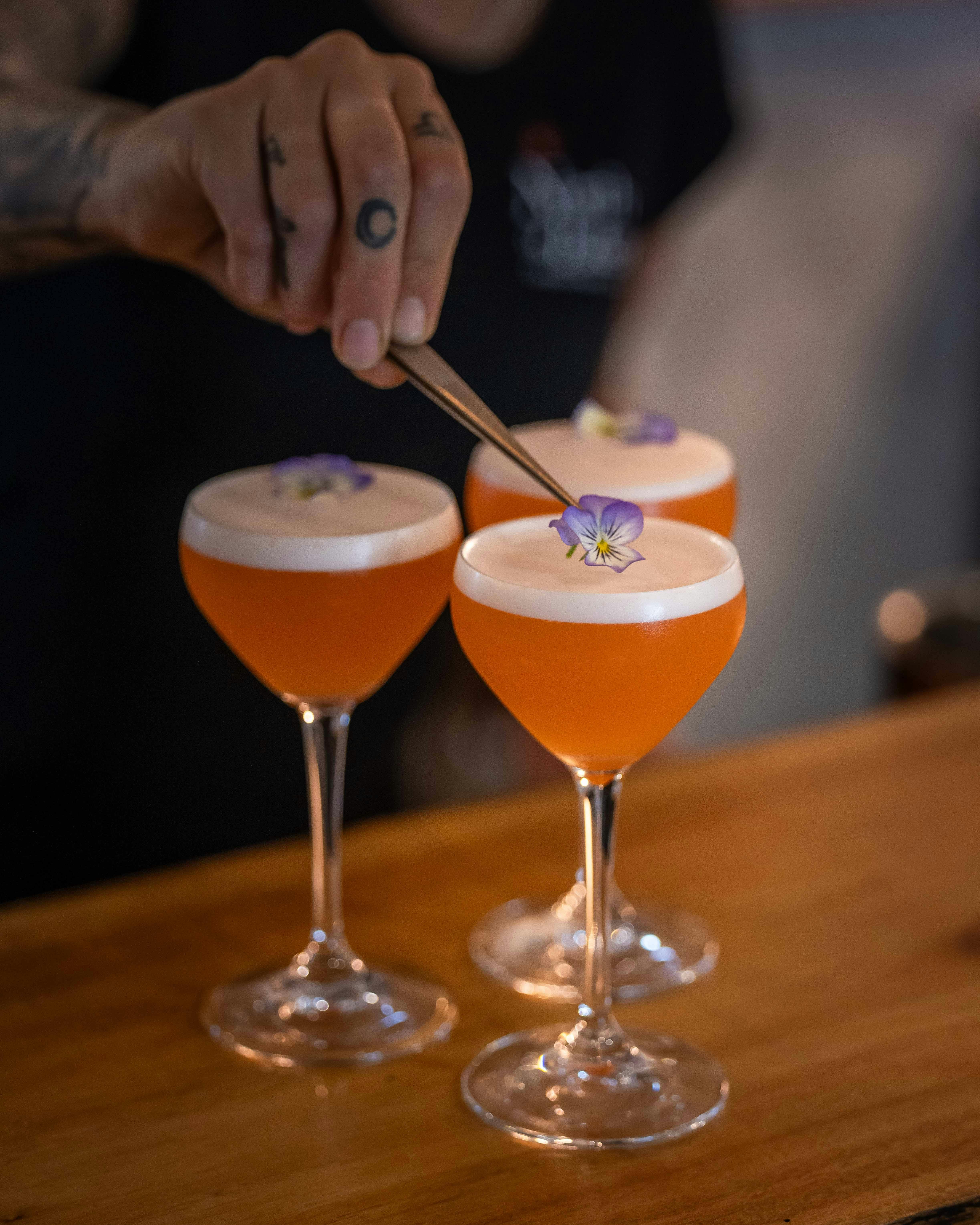 Picture of woman adding floral garnish to three cocktails