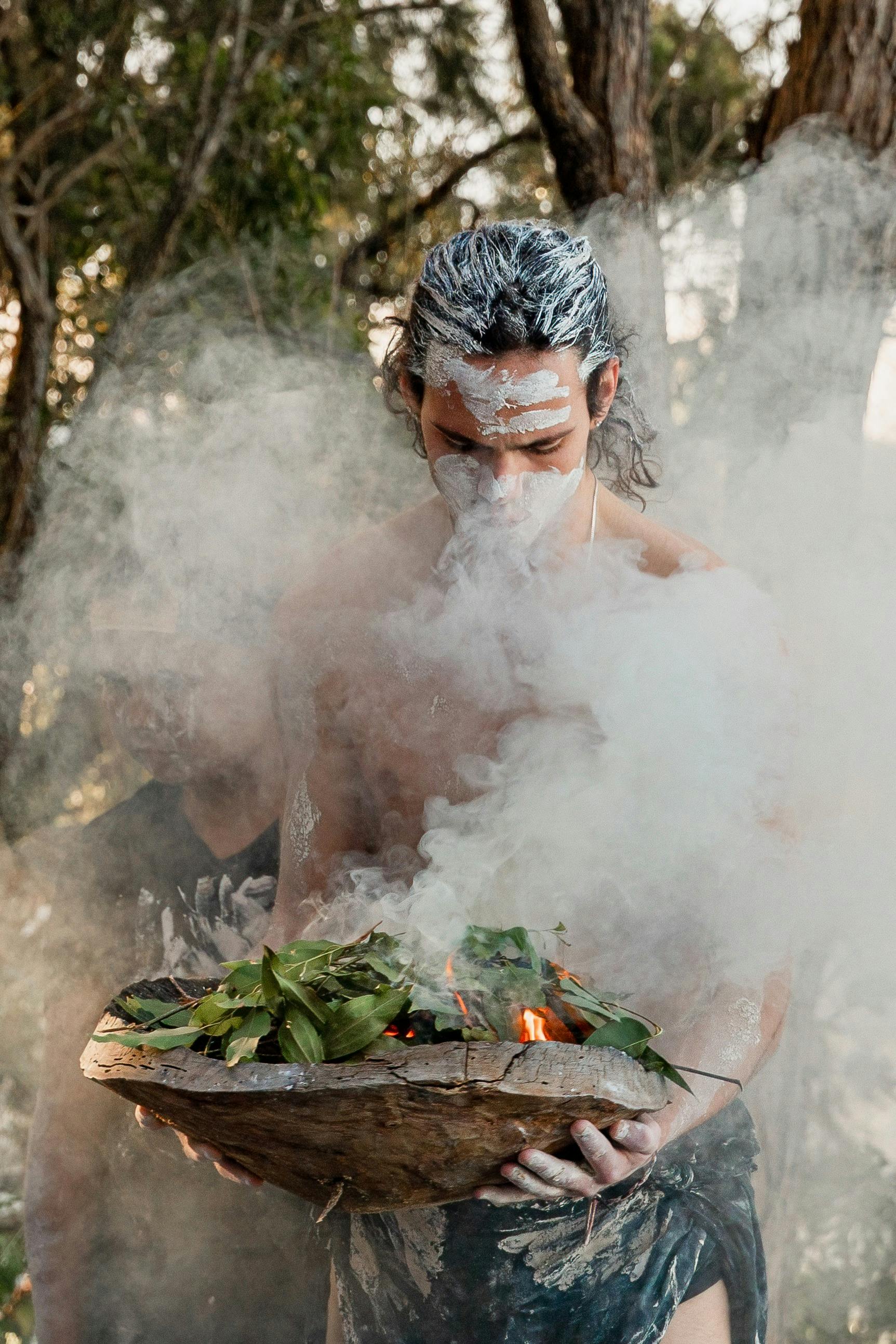 Indigenous Man holding fire in a wooden bowl in order to perform the Smoking Ceremony with guests