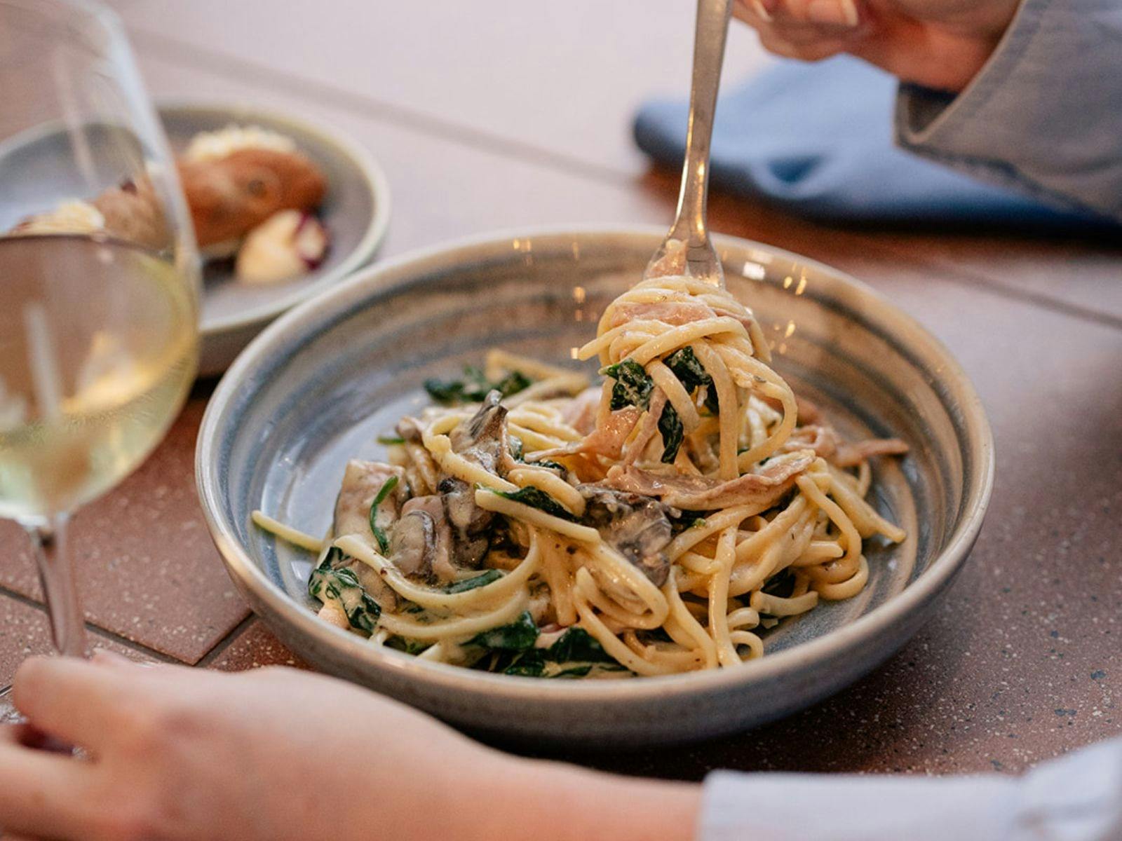 Pasta in a bowl being twirled on a fork with a glass of white wine