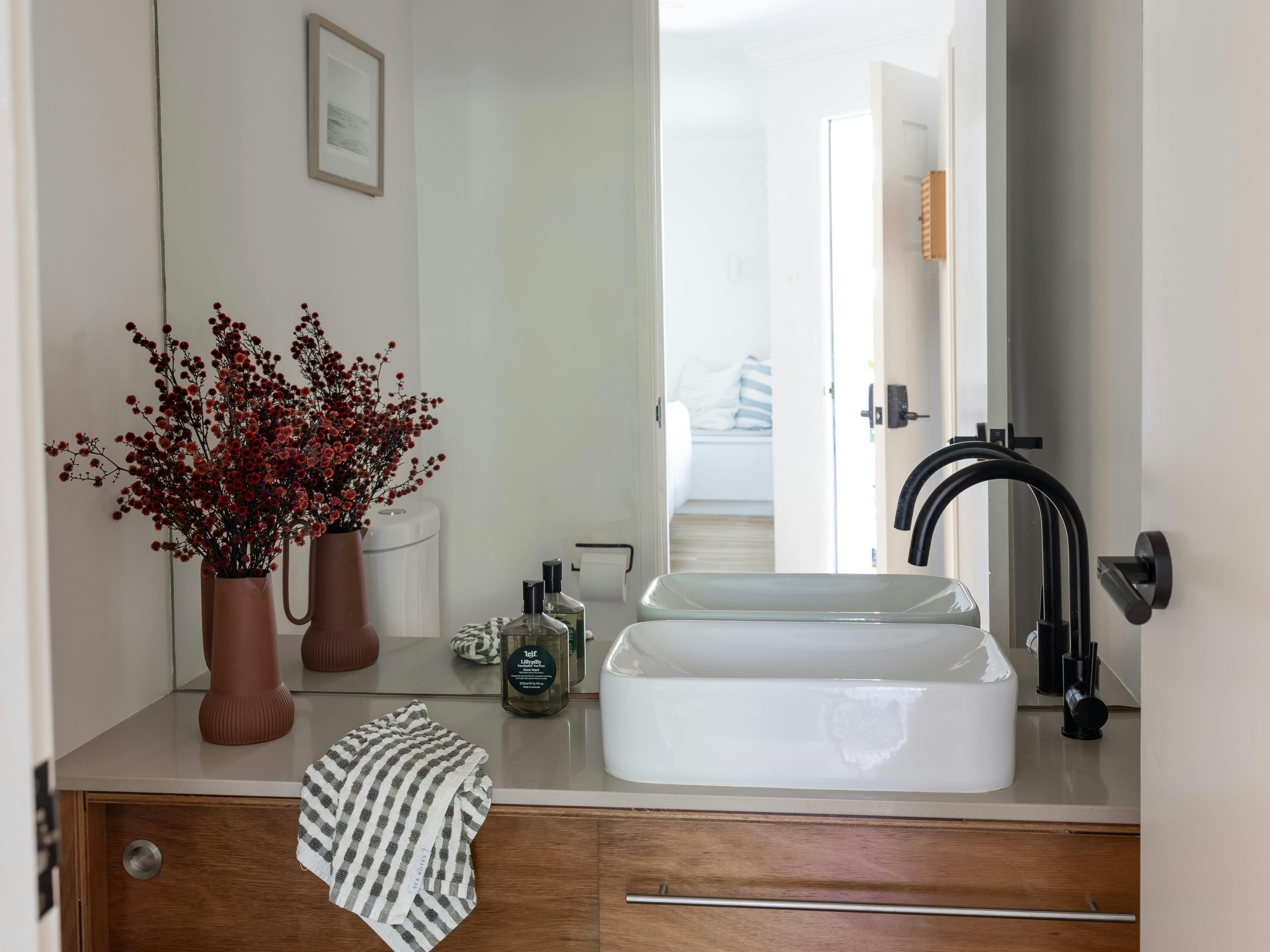 Bright powder room with gloss white basin on a timber vanity with draped hand towel and red floral