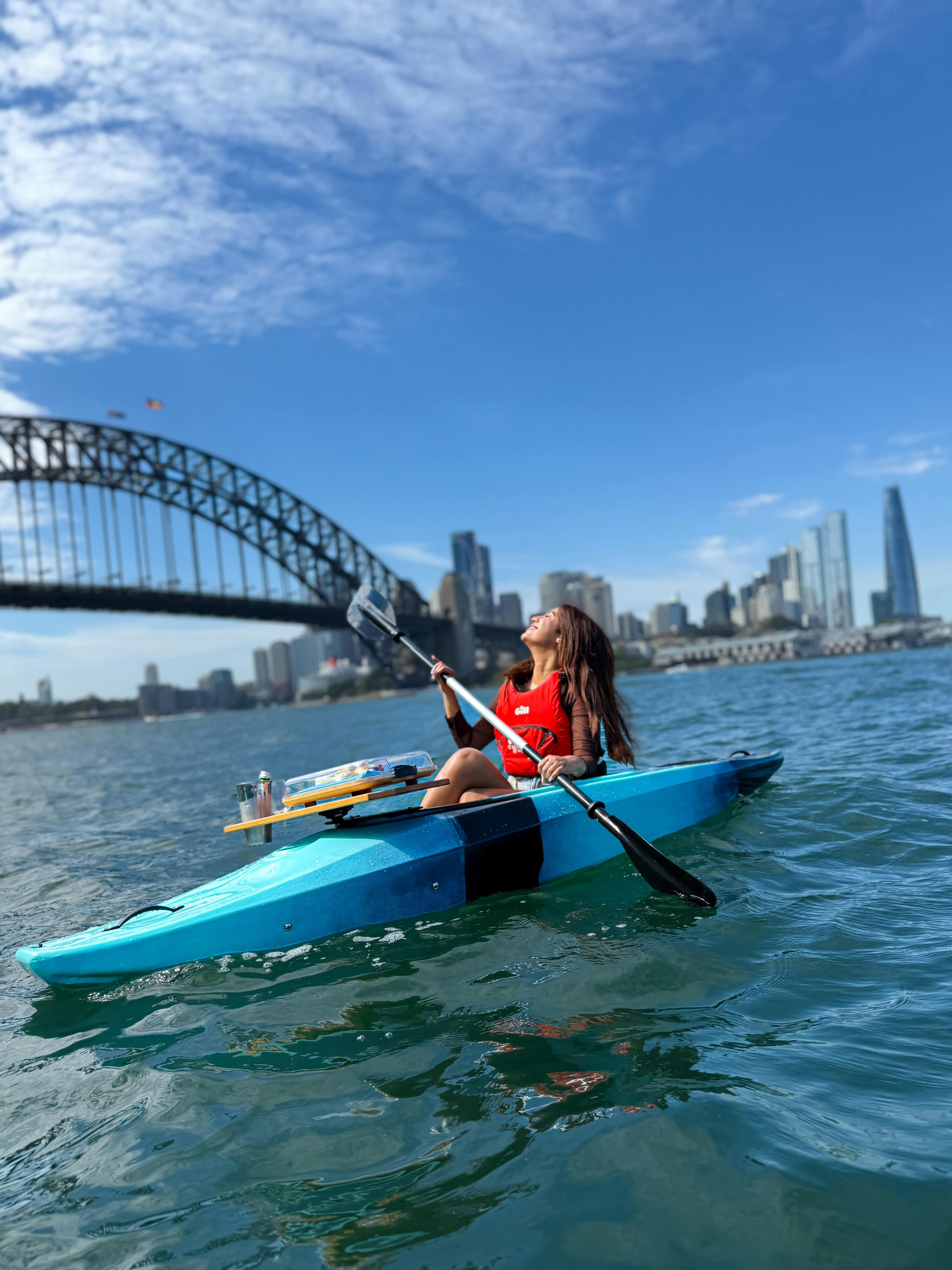 Lady embracing sun on her face while paddling on kayak with scones and tea attached to front.