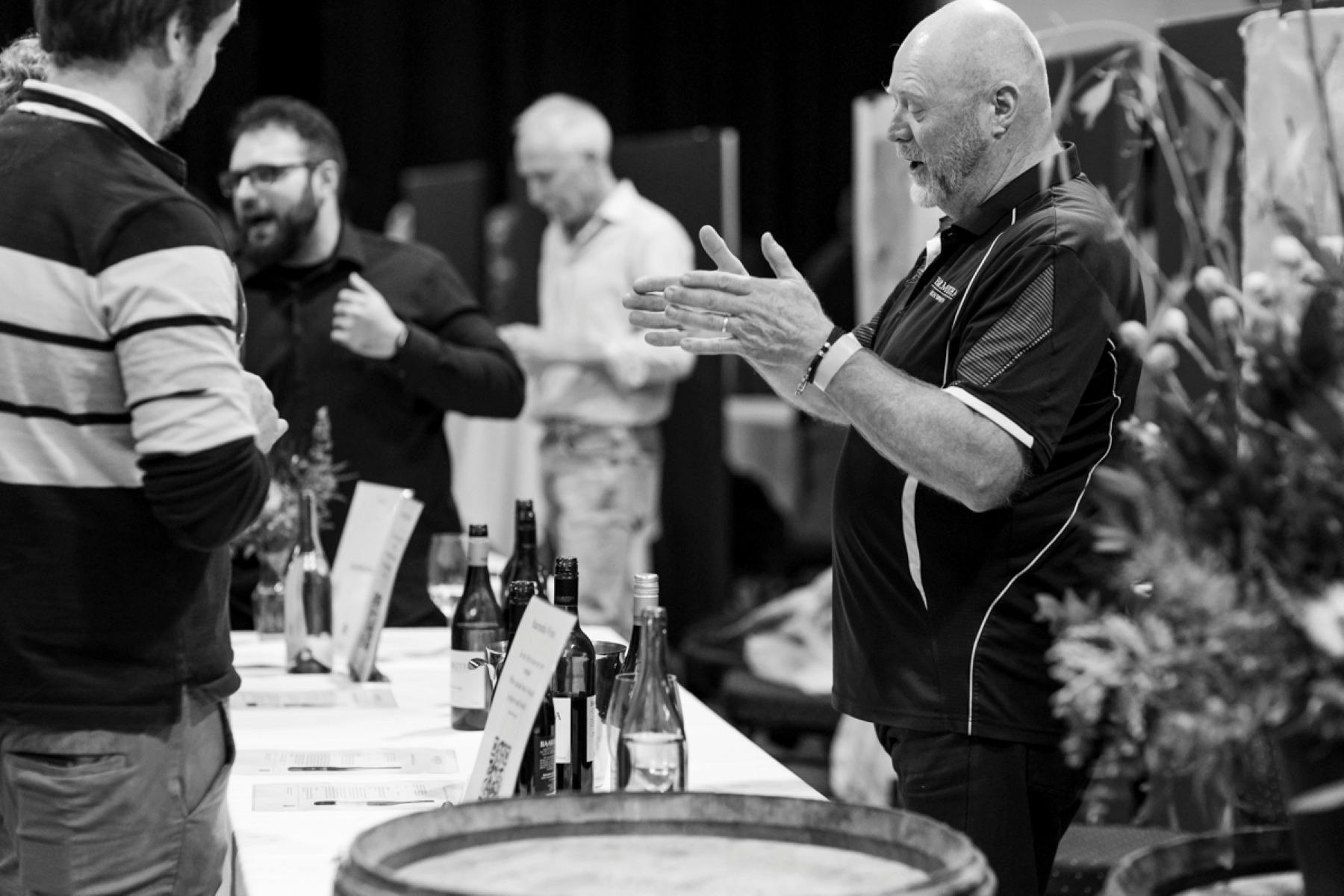Man describing wine to two visitors at a wine tasting event
