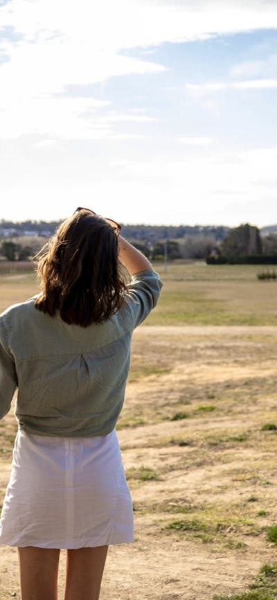 A tourist stands at a lookout, viewing vast open bush-covered fields stretching into the distance