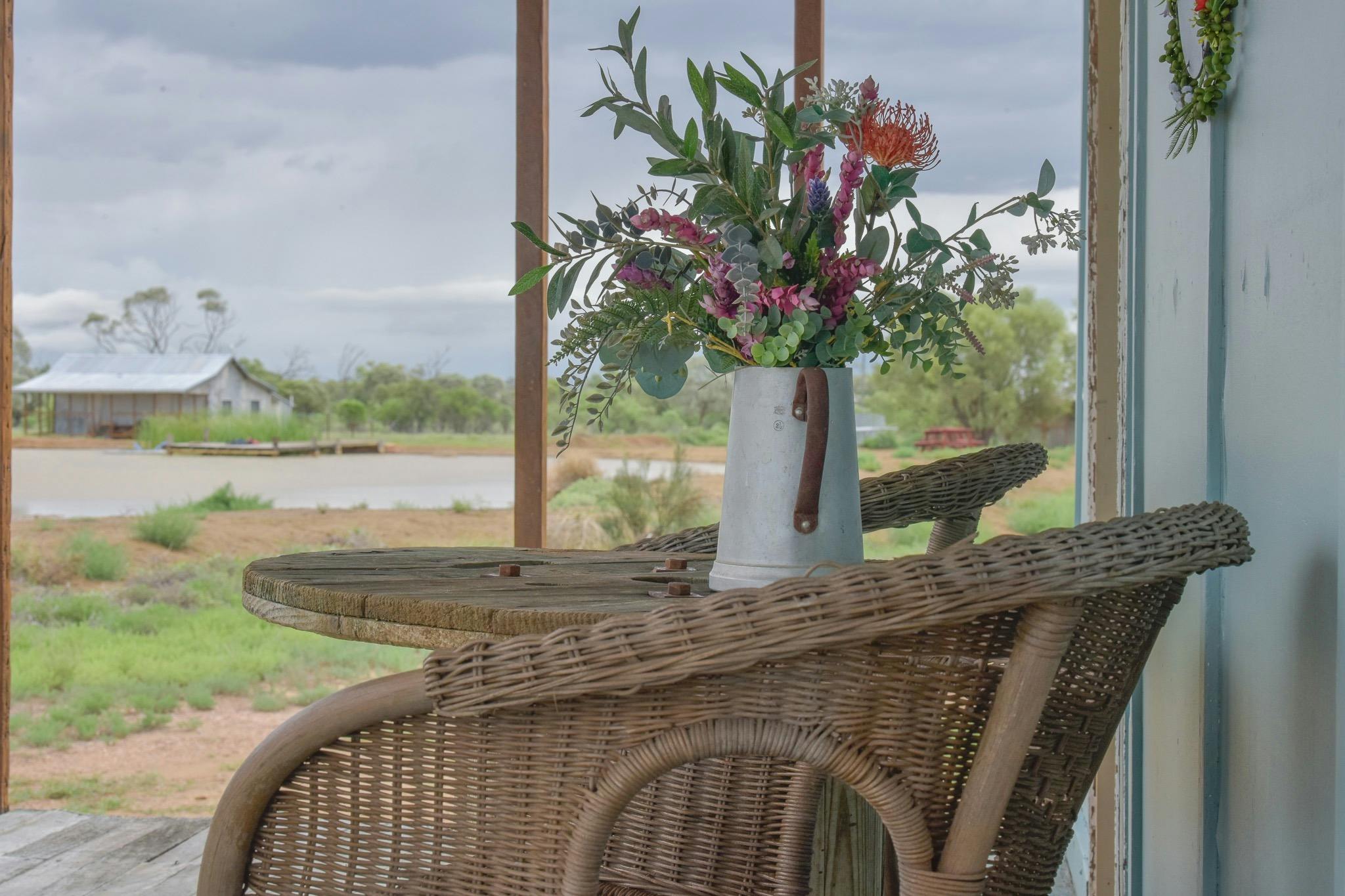 two chairs on a deck with a vase of flowers overlooking a small body of water