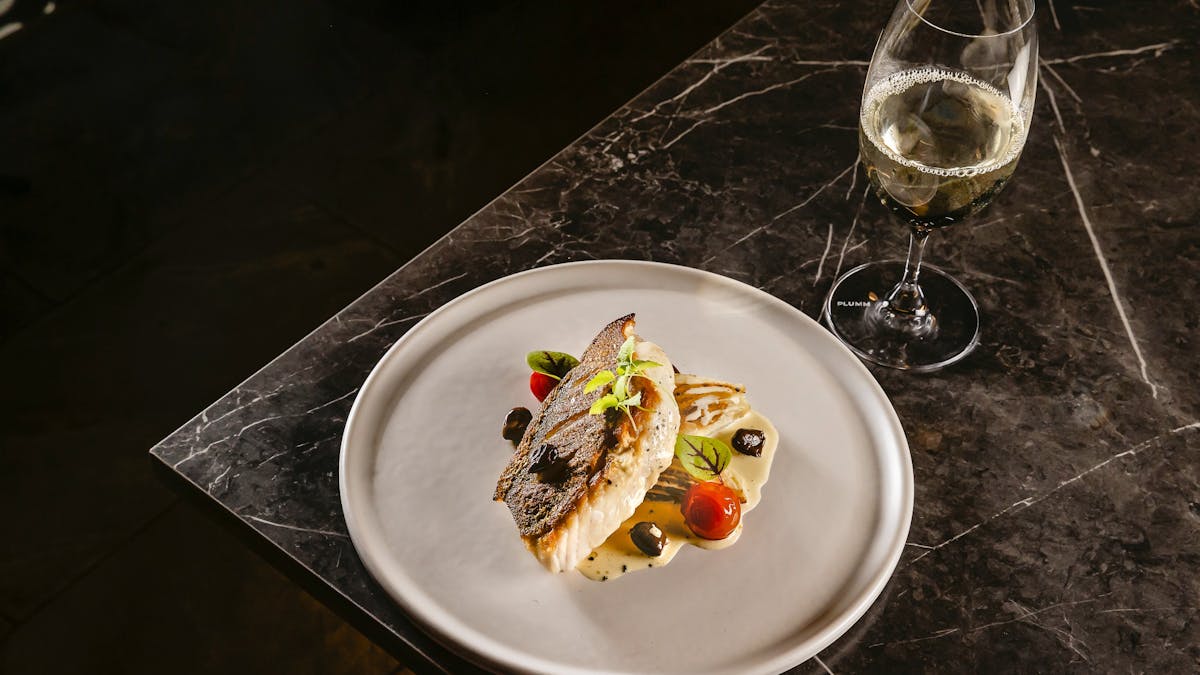 White plate with Murray River cod in a dark table and a glass of white wine on the right