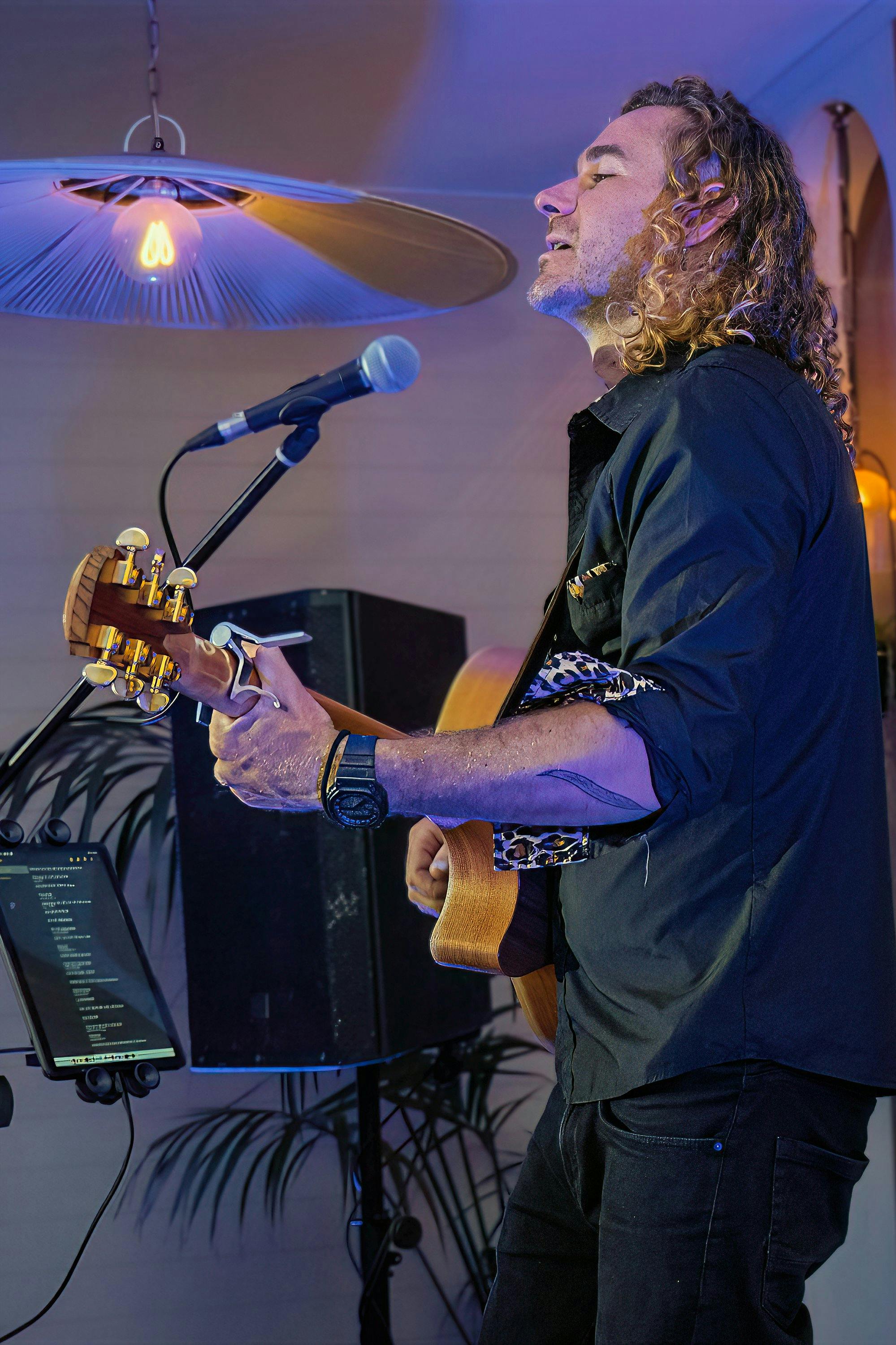 A blonde guitarist is performing - we see his profile as he sings into a microphone