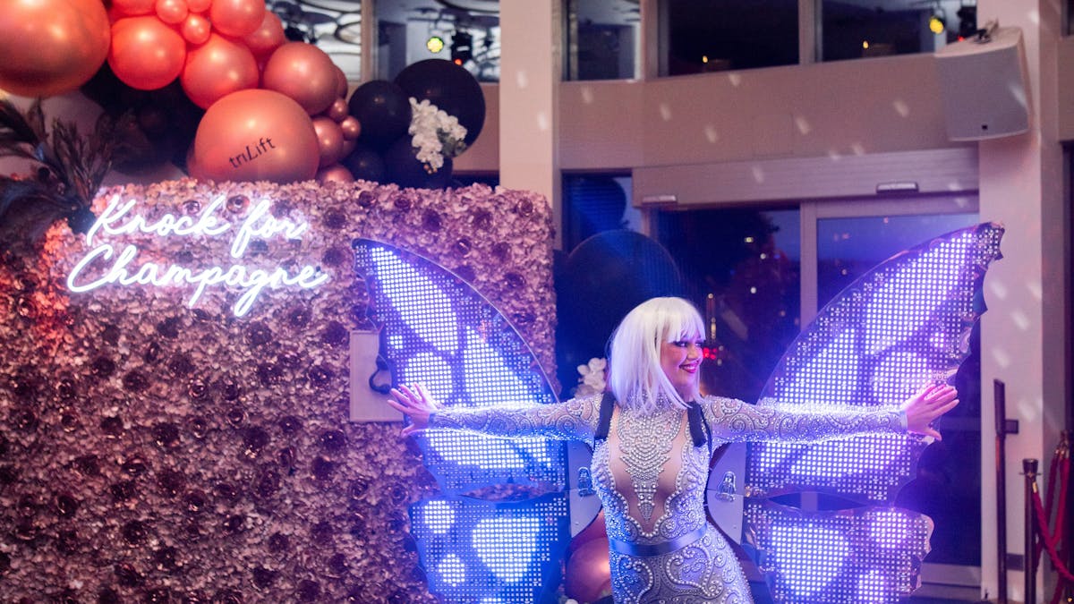 A performer wears a silver unitard costume and has giant LED wings on her shoulders.
