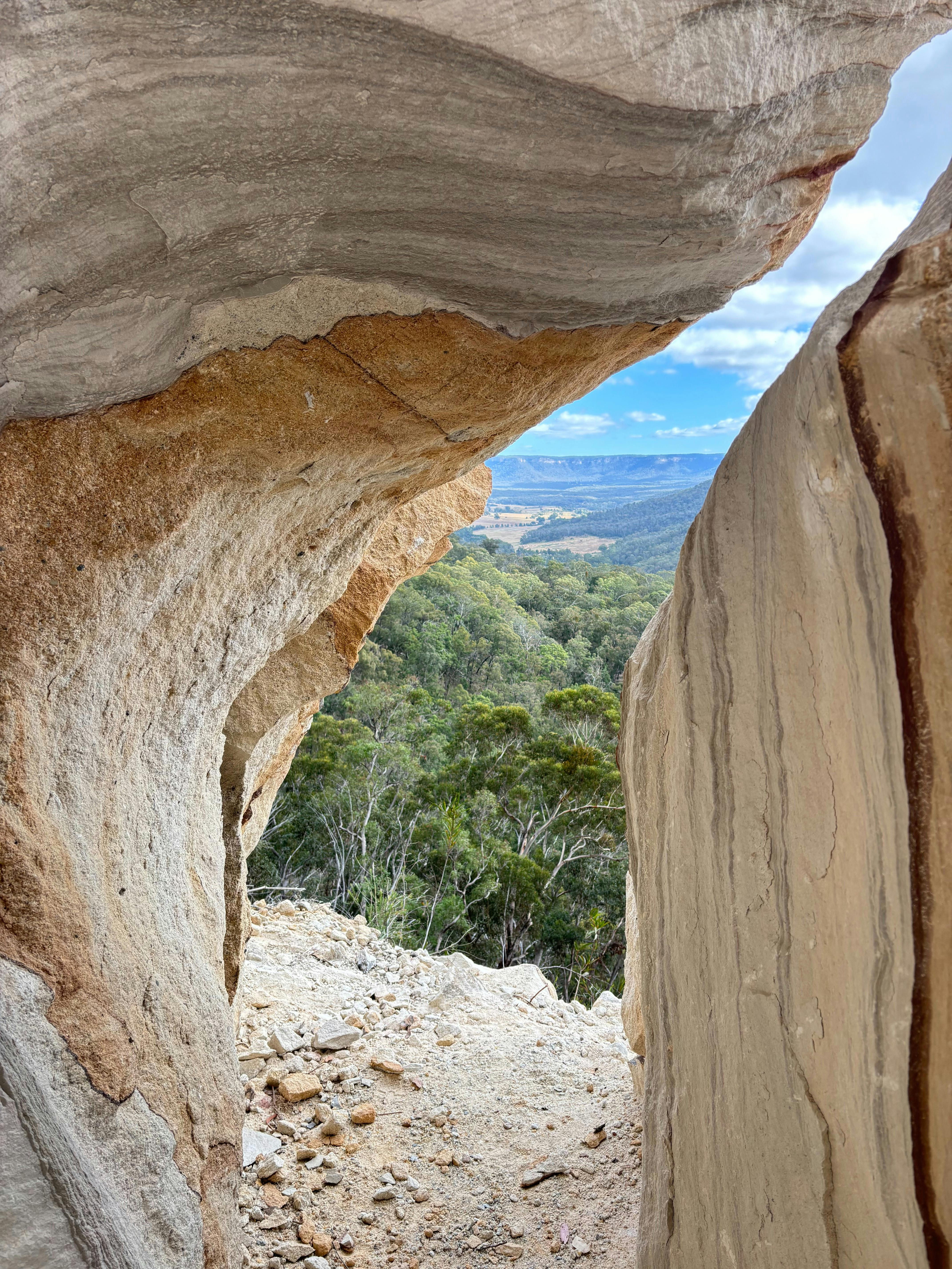 A crack between two large sandstone boulders which provides a view of the valley below.