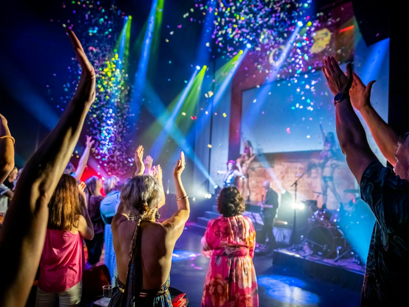 A lively concert scene with a crowd enjoying music as colourful confetti falls from above. A lively concert scene with a crowd enjoying music as colourful confetti falls from above.