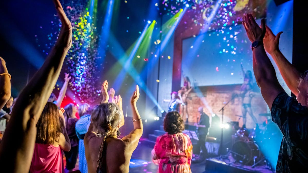 A lively concert scene with a crowd enjoying music as colourful confetti falls from above.