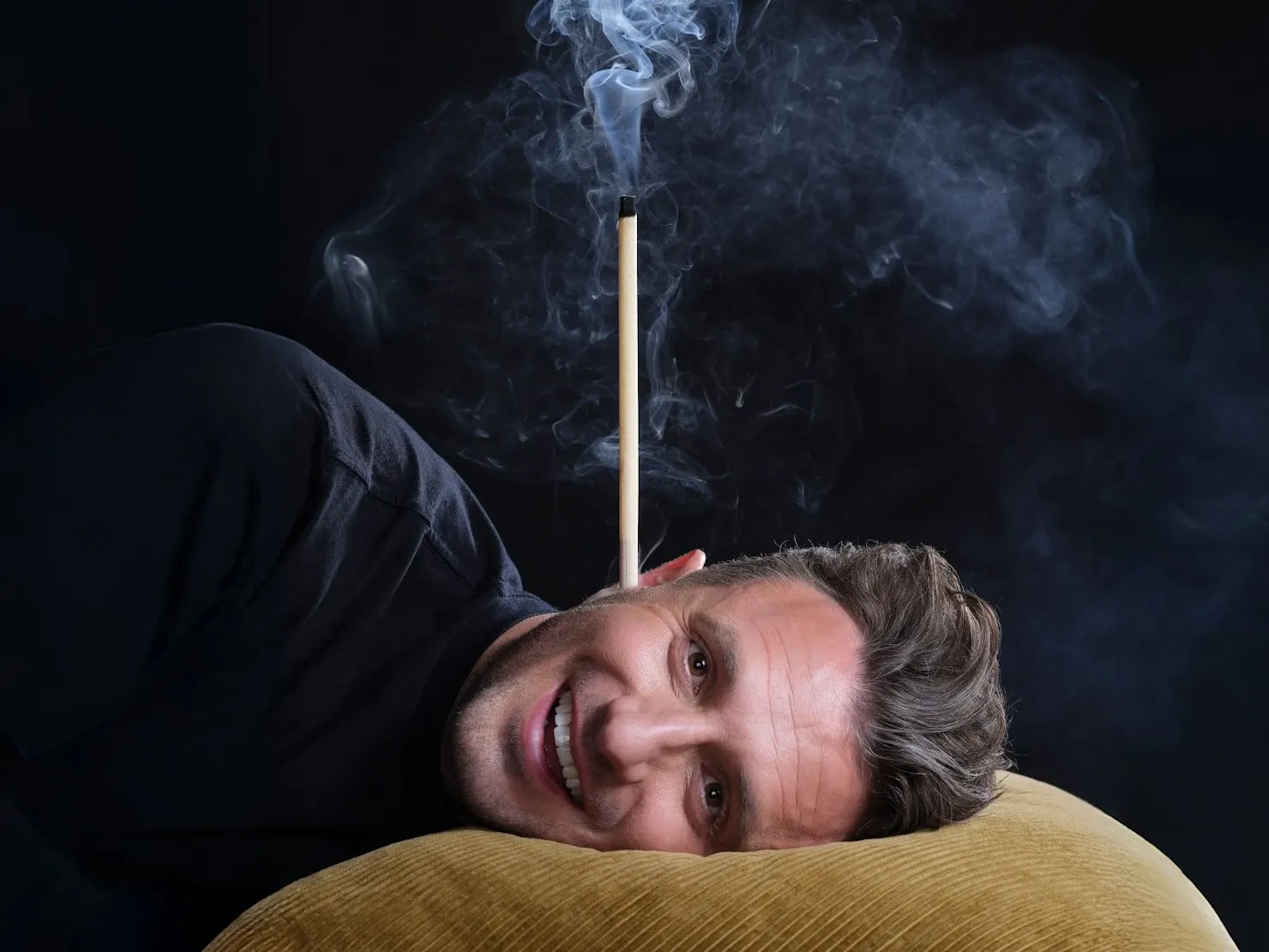 Tommy lying with his head on a mustard coloured pillow with an incense stick burning behind