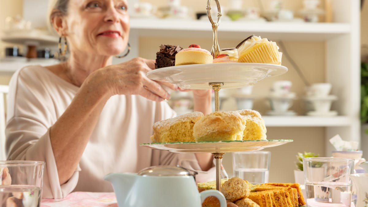 Lady sitting at a table with a high tea trio stand in the foreground