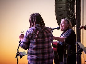 Man and woman singing on stage while sun is setting