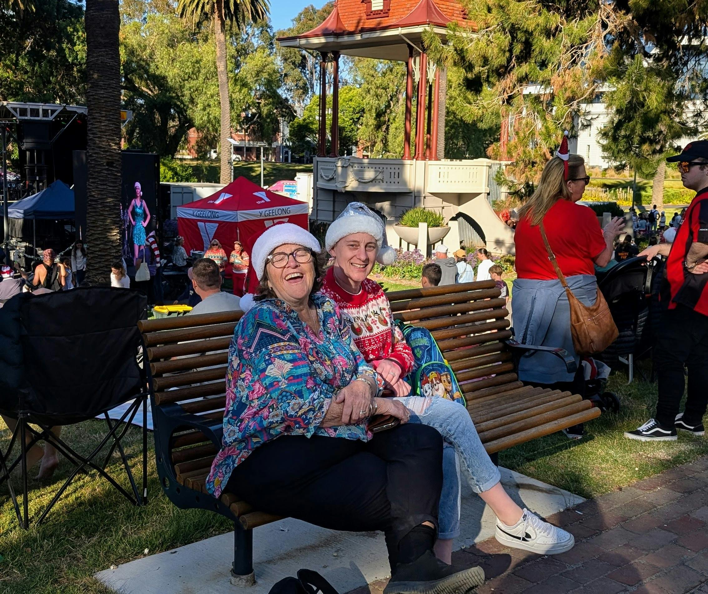 two adults with santa hats on  sitting on bench at Carols by Candlelight