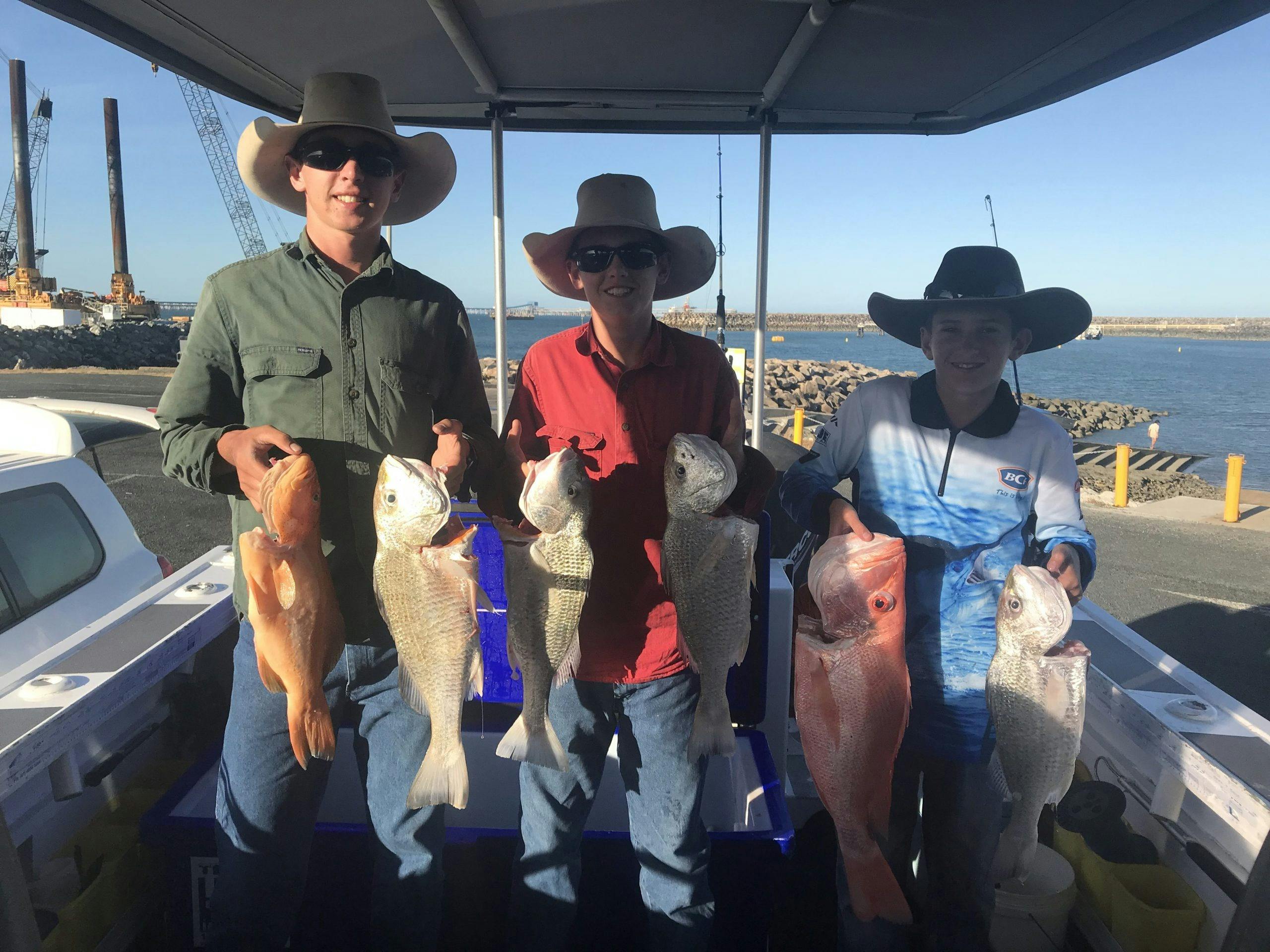 3 young boys hold 2 fish each that they have caught, Standing in the boat at  the boat Ramp.