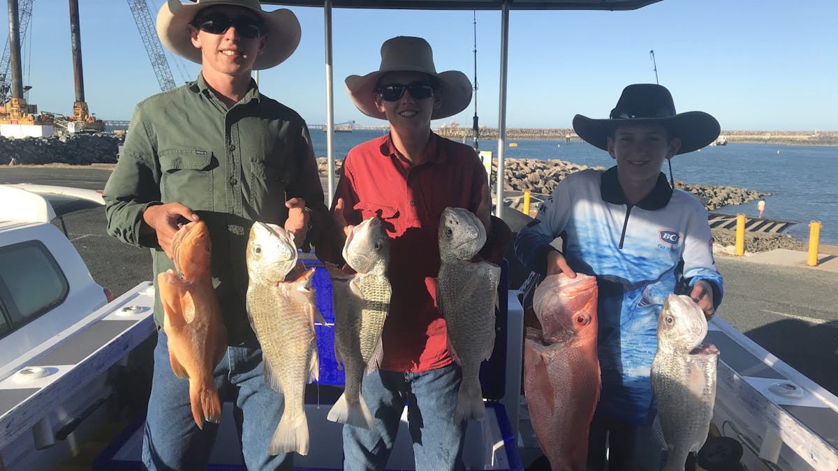 3 young boys hold 2 fish each that they have caught, Standing in the boat at  the boat Ramp.