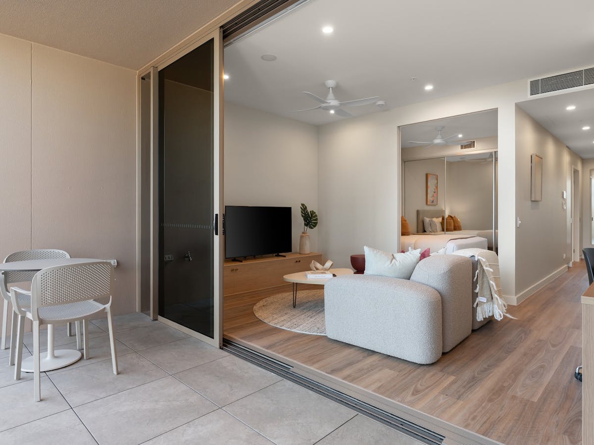 Tiled balcony with 2-seater outdoor dining set, looking into living room of apartment.