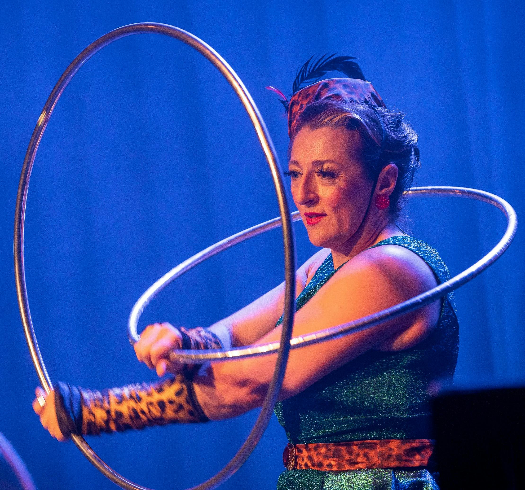 Glamorous woman in 1950s green wiggle dresss and leopard print pillbox hat and gloves holding hoops