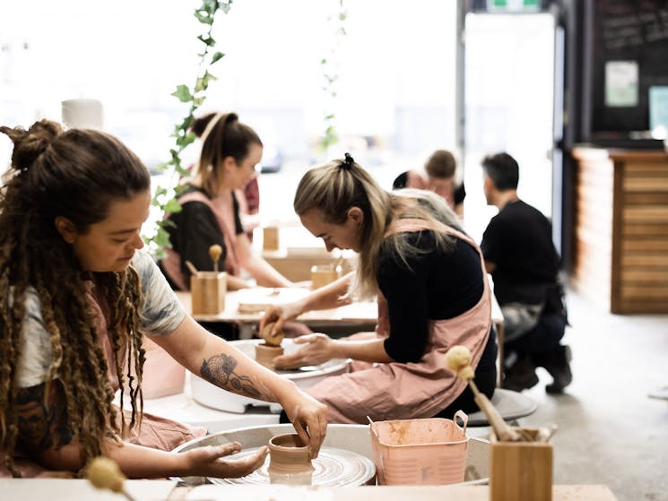 Picture of a group of people sitting at a pottery wheel making pots with clay a