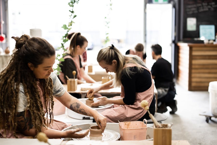 Picture of a group of people sitting at a pottery wheel making pots with clay a