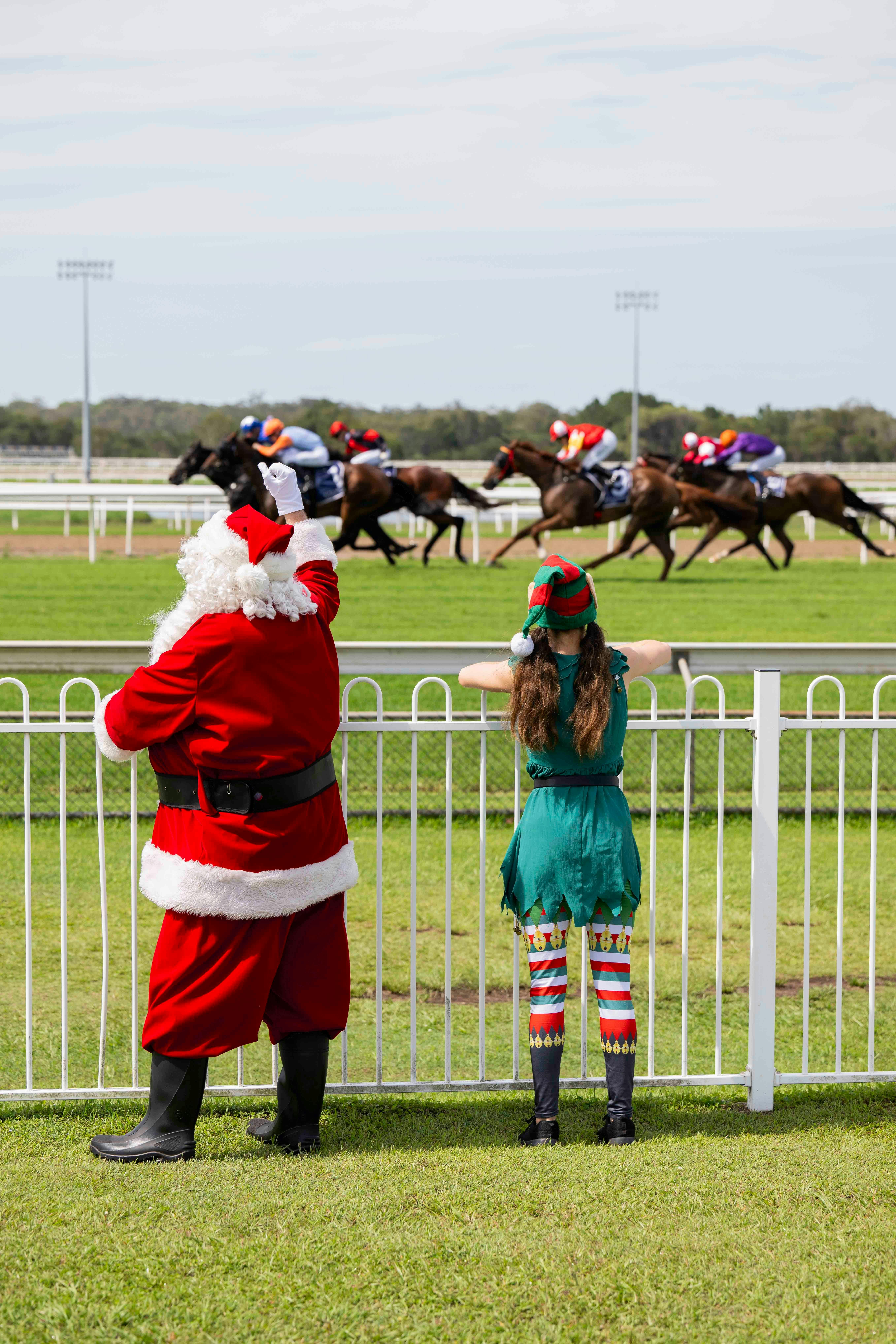 Santa and Elf cheering on the thoroughbred horses from the fence line