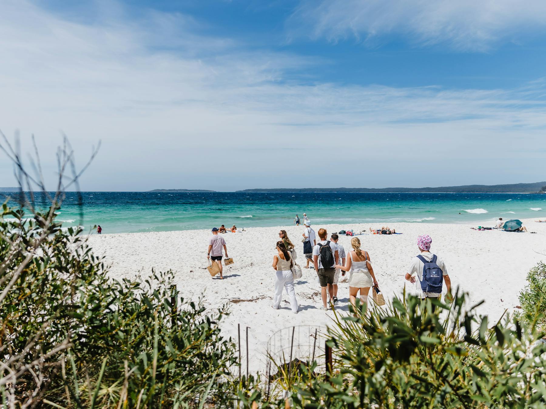 People walking onto a beach with white sane and blue sky