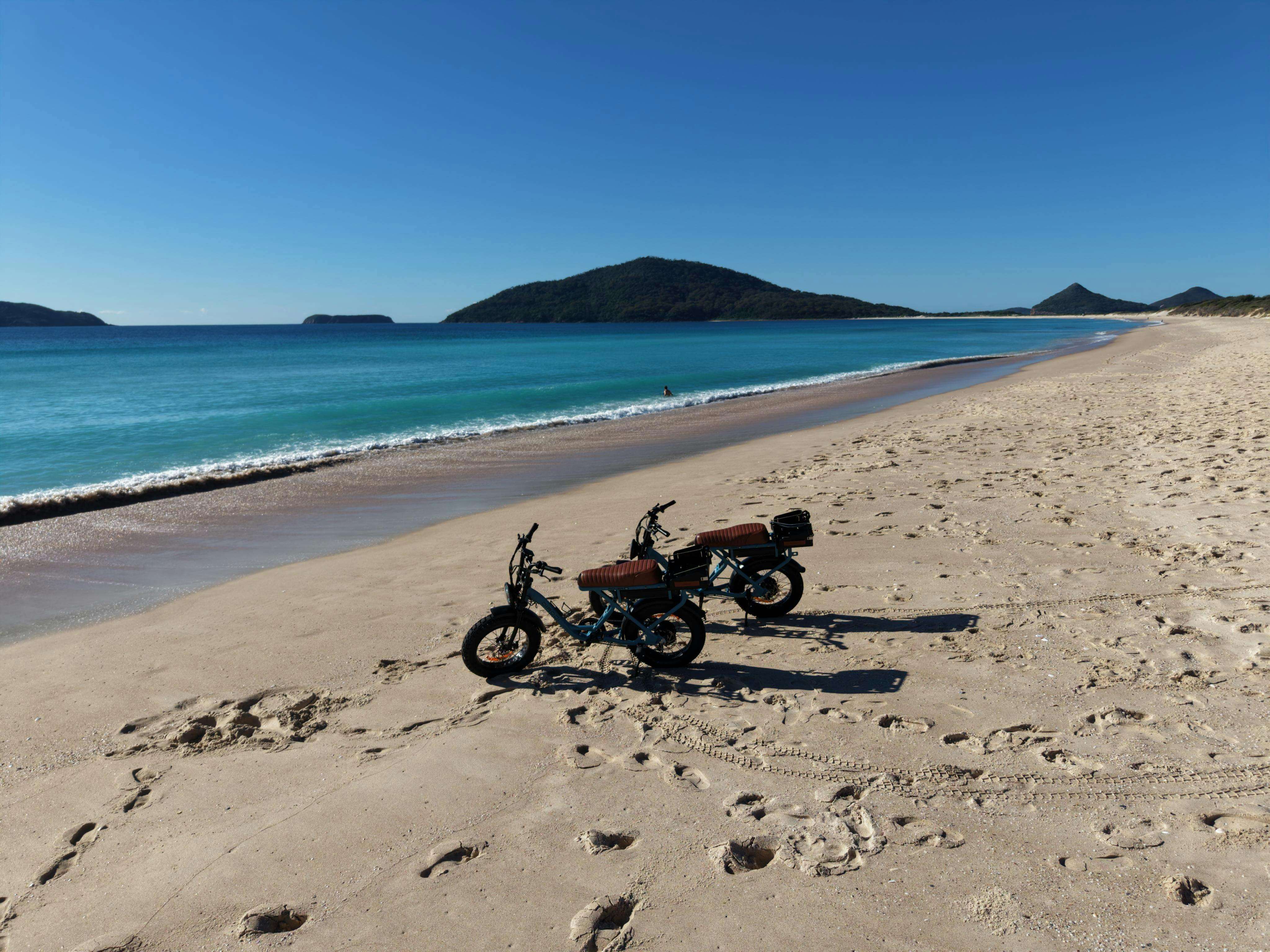 e-bikes on Bennets beach,  Hawks nest, with Yacaaba Head in back ground