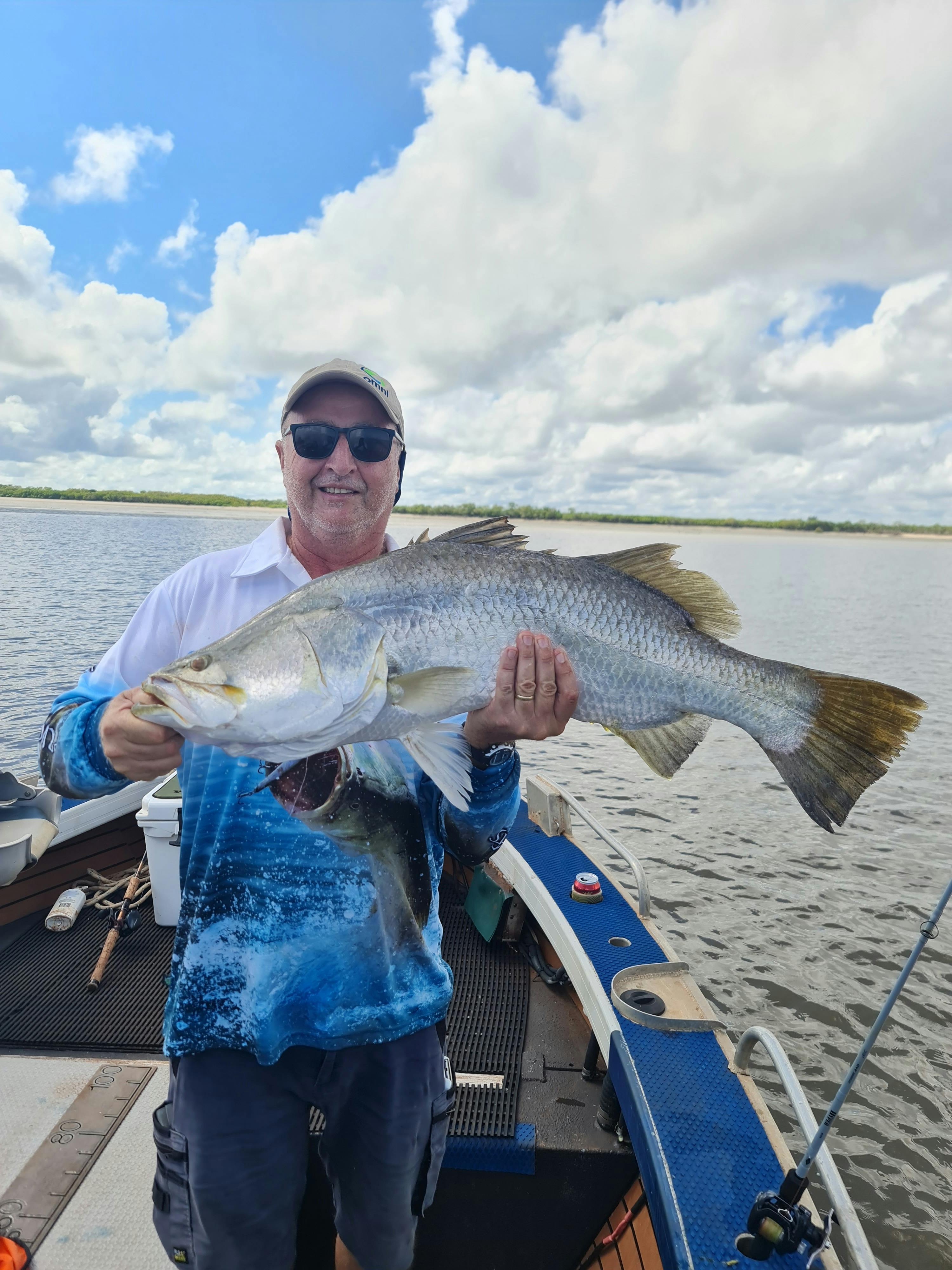 Tony standing in a boat holding his 99cm barramundi.