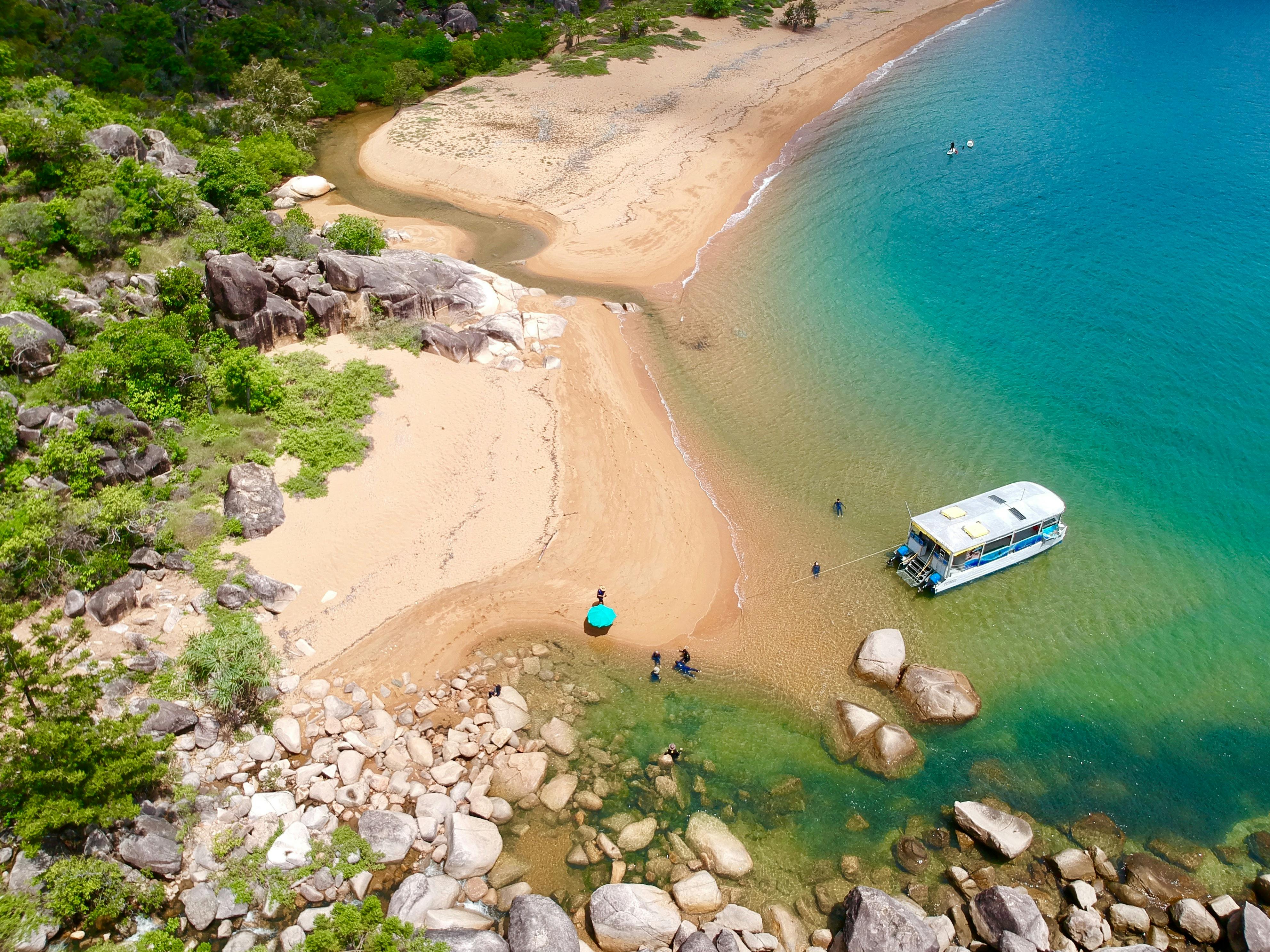 drone picture of boat on a secluded sandy beach with blue water and guests swimming