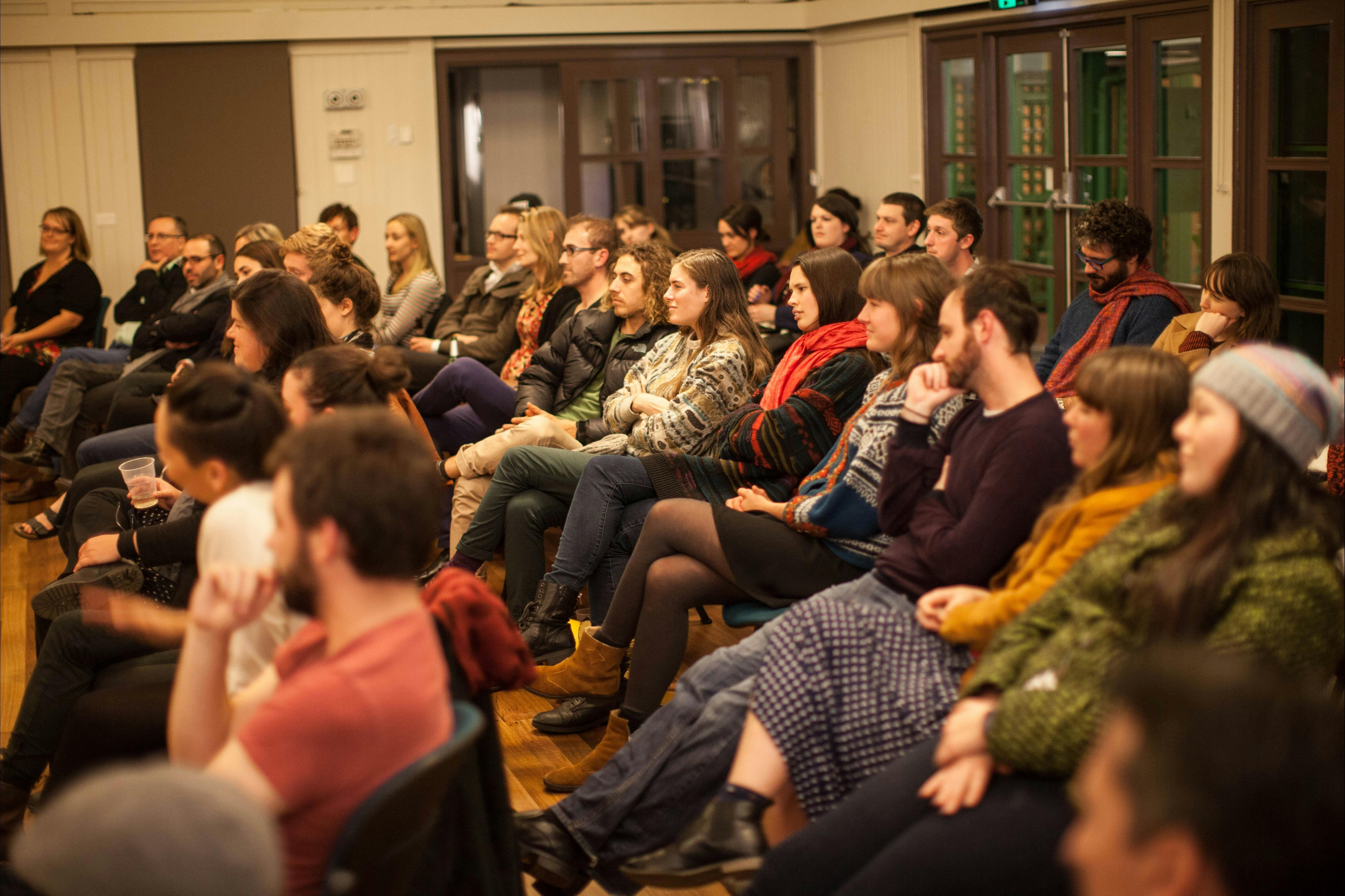 A crowd of seated people watching a poetry performance (performer outside of the frame)