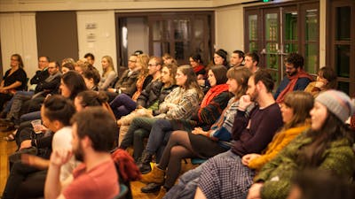 A crowd of seated people watching a poetry performance (performer outside of the frame)
